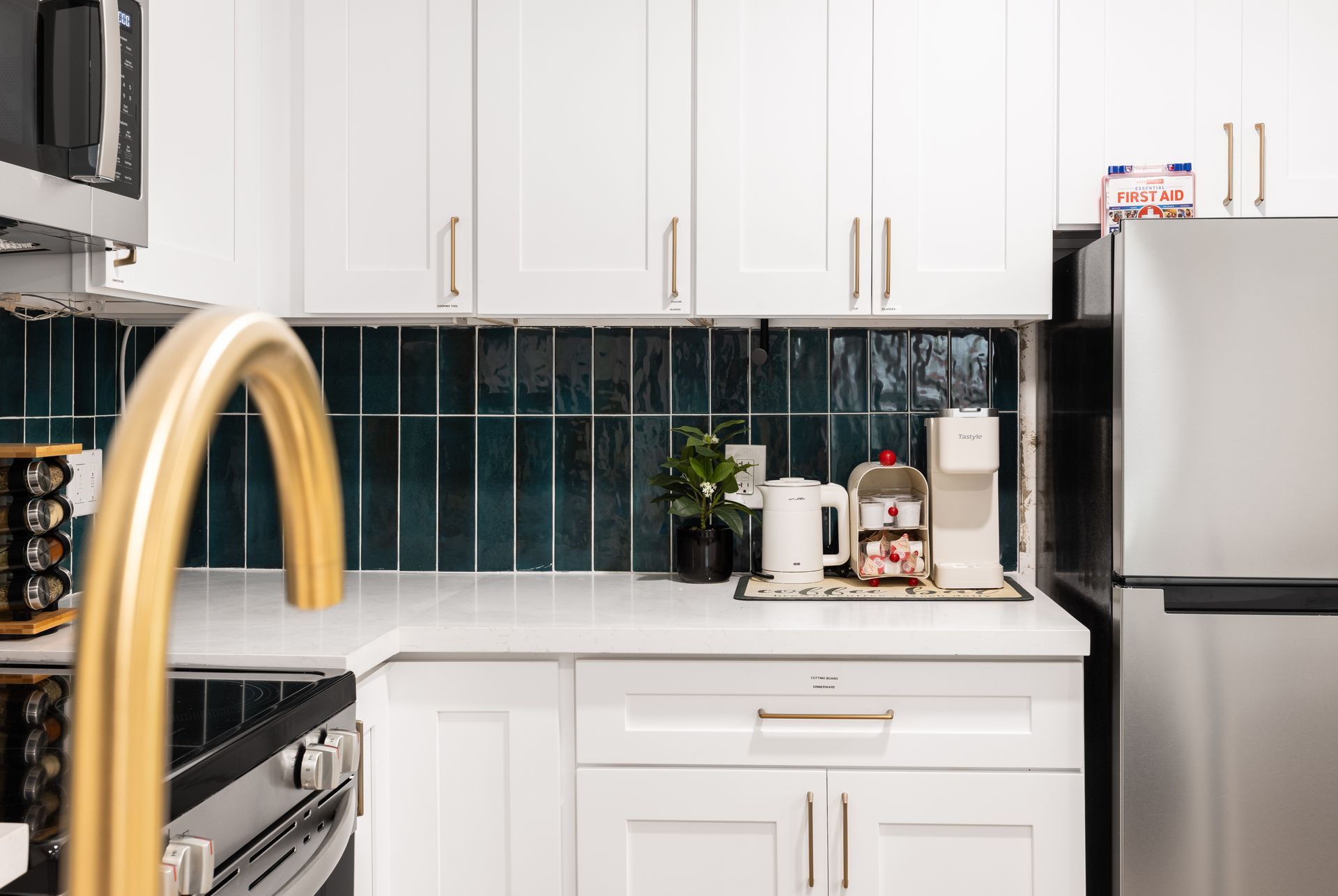 Modern kitchen with white cabinets, dark tile backsplash, stainless fridge, and gold faucet on a white countertop