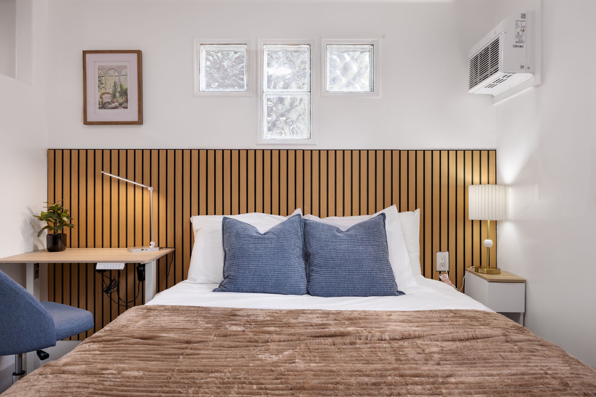Bright modern bedroom with striped wood headboard, blue pillows, white walls, and a fur throw on the bed