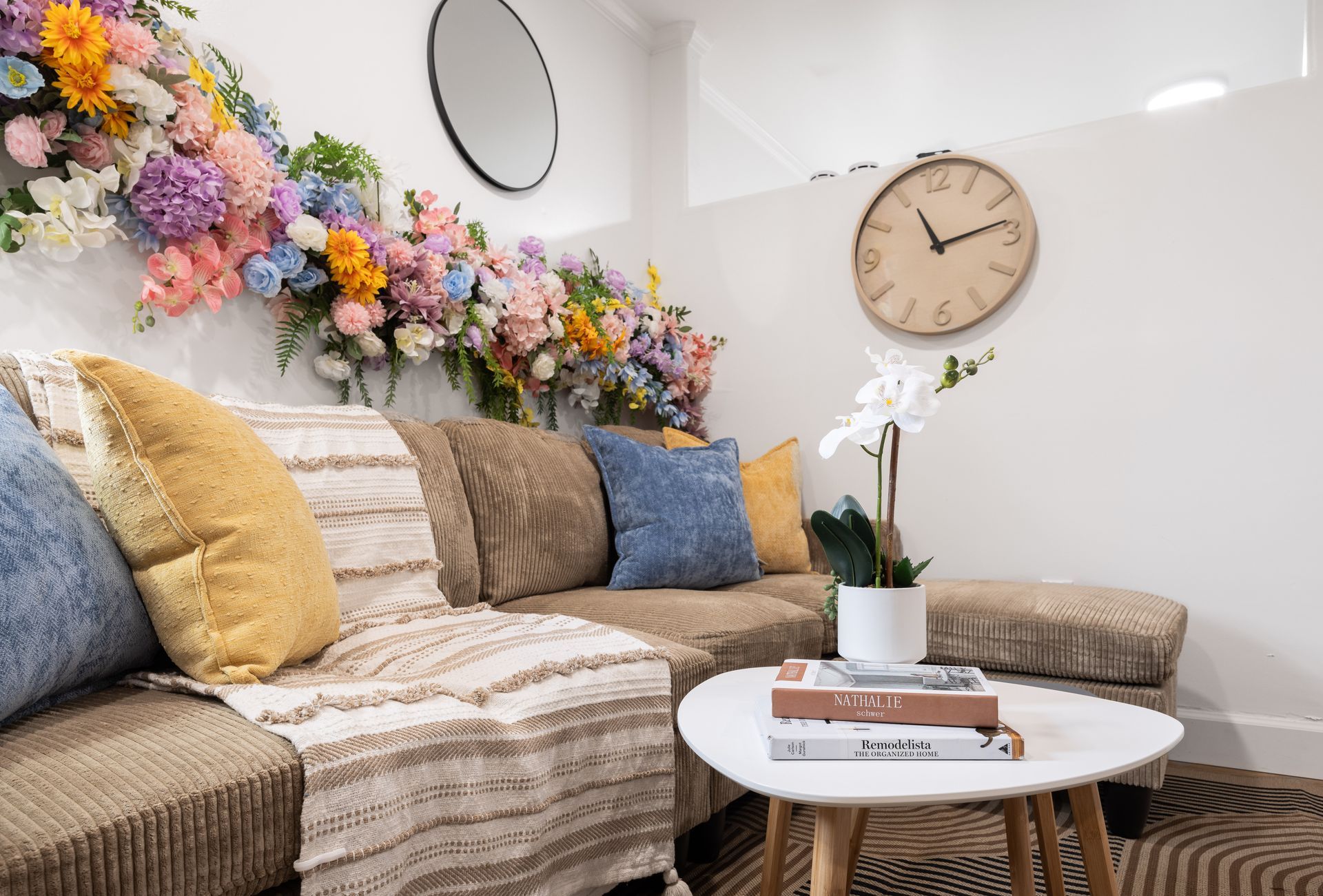 Cozy living room with floral wall decor, beige sofa, round mirror, clock, and white coffee table