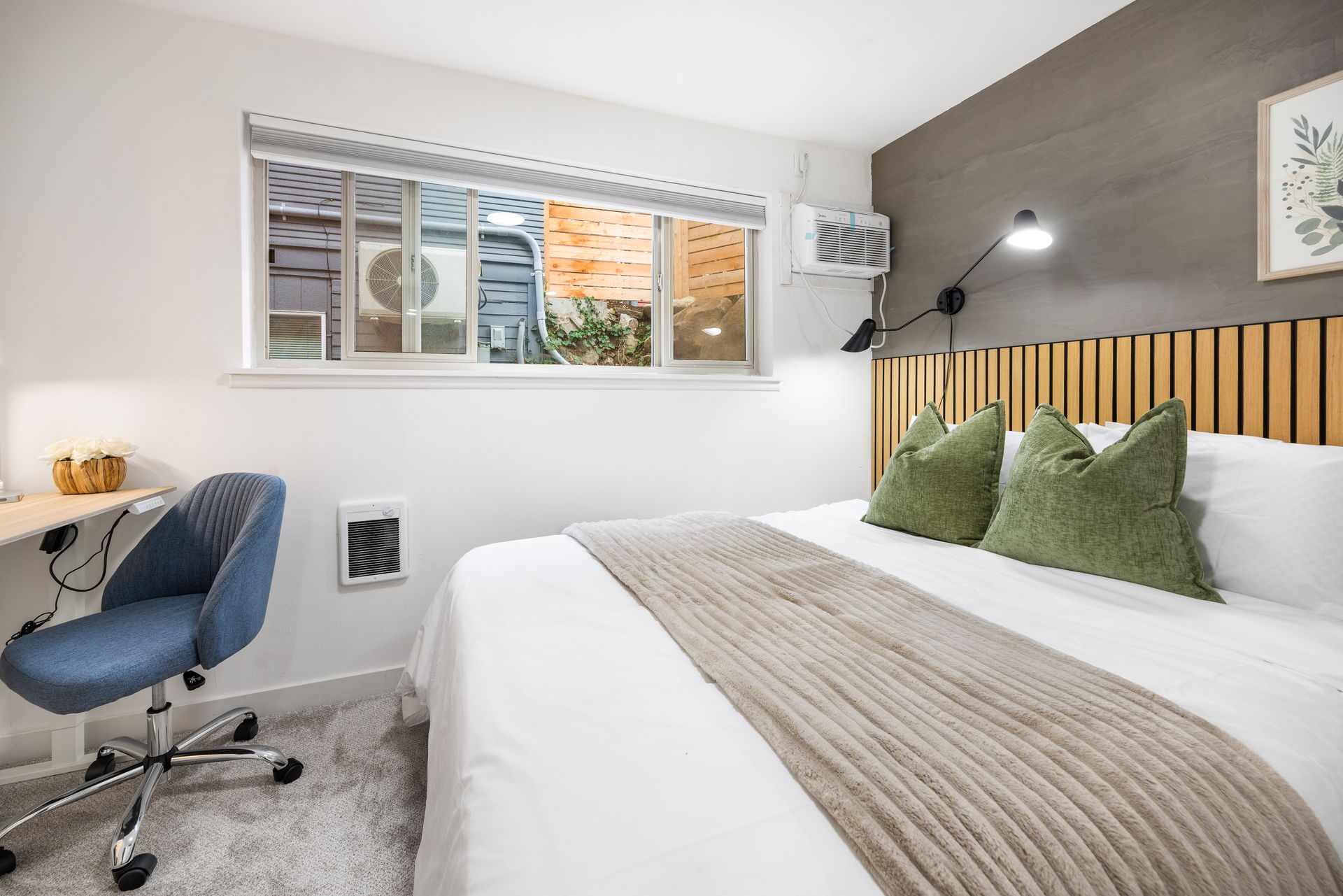 Bright bedroom with white bed, gray chair, desk, and window nook with green pillows