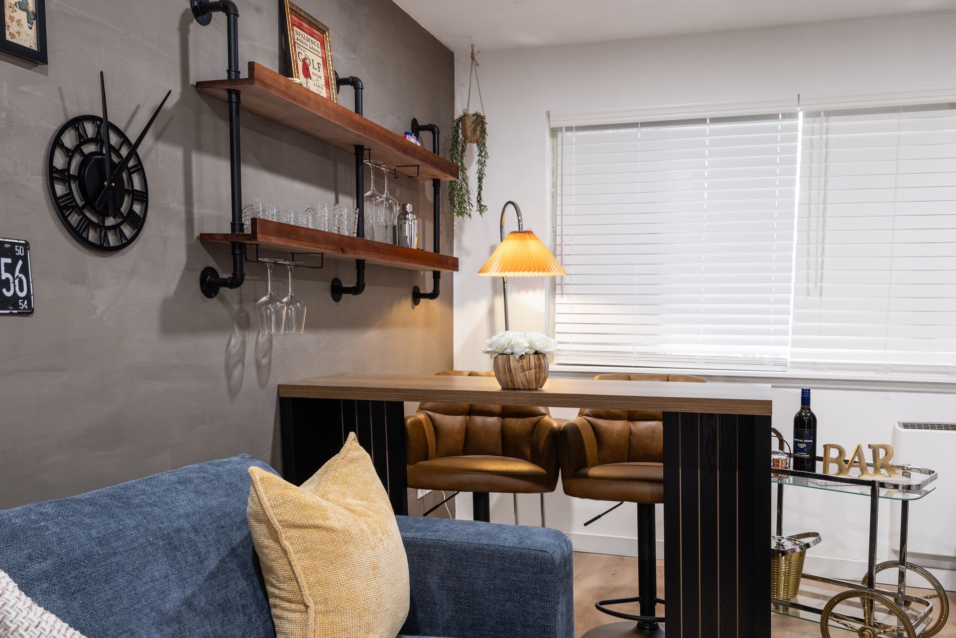 Cozy home office with desk, lamp, wall shelves, blue sofa, and window blinds
