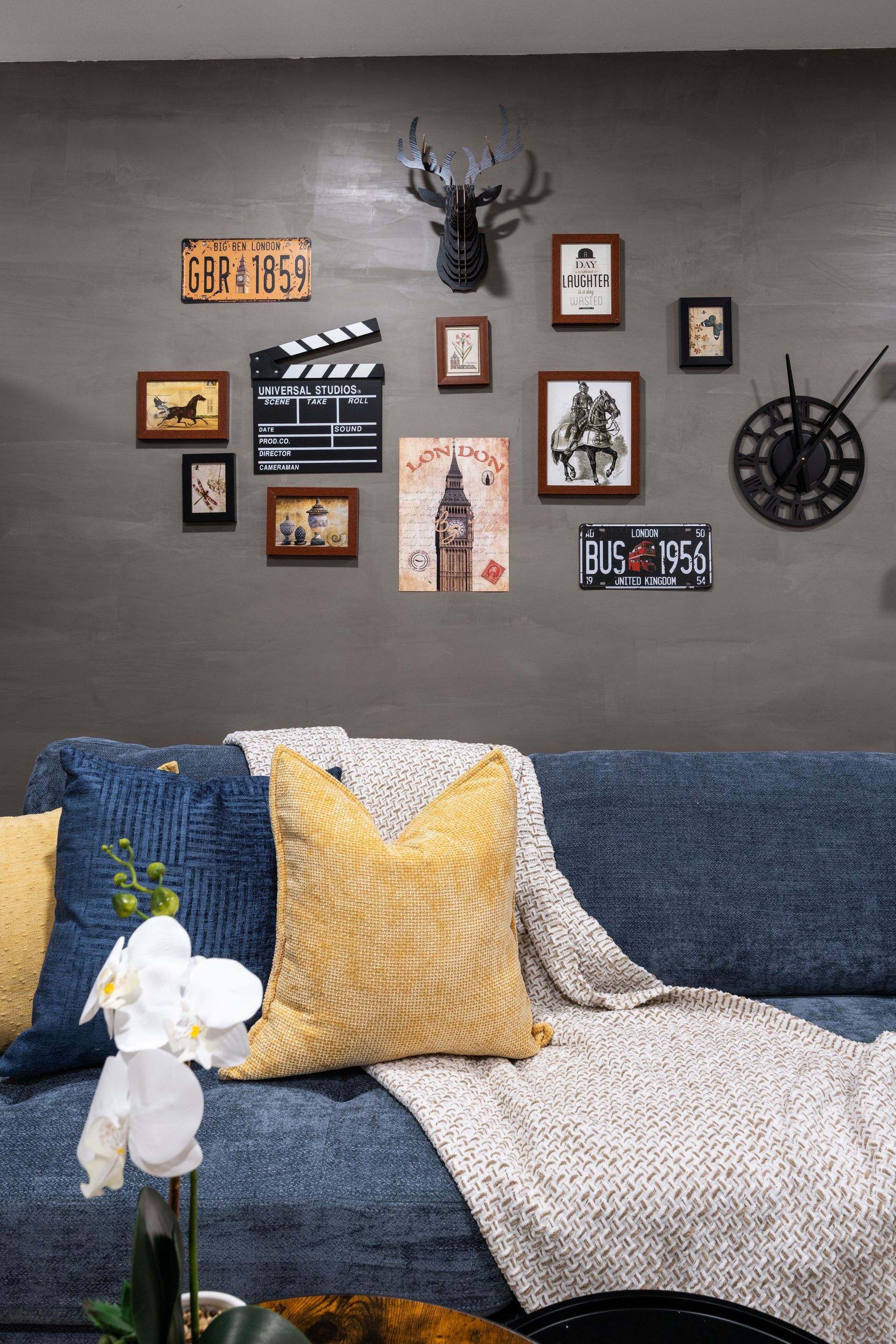Cozy living room wall with framed art and decor above a blue couch with yellow and white pillows.