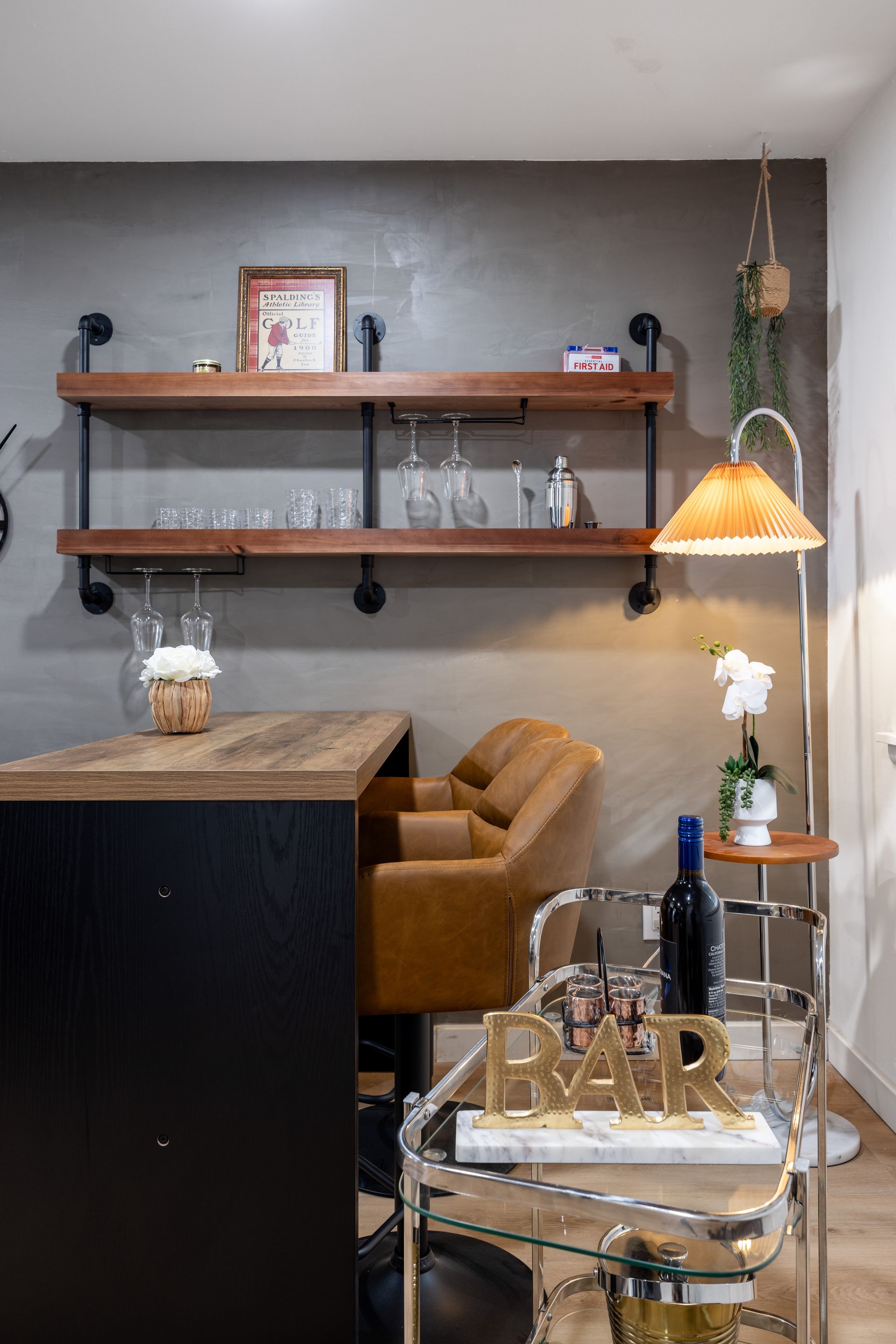 Cozy bar nook with wood shelves, tan chair, marble table, and warm hanging lamp against a gray wall