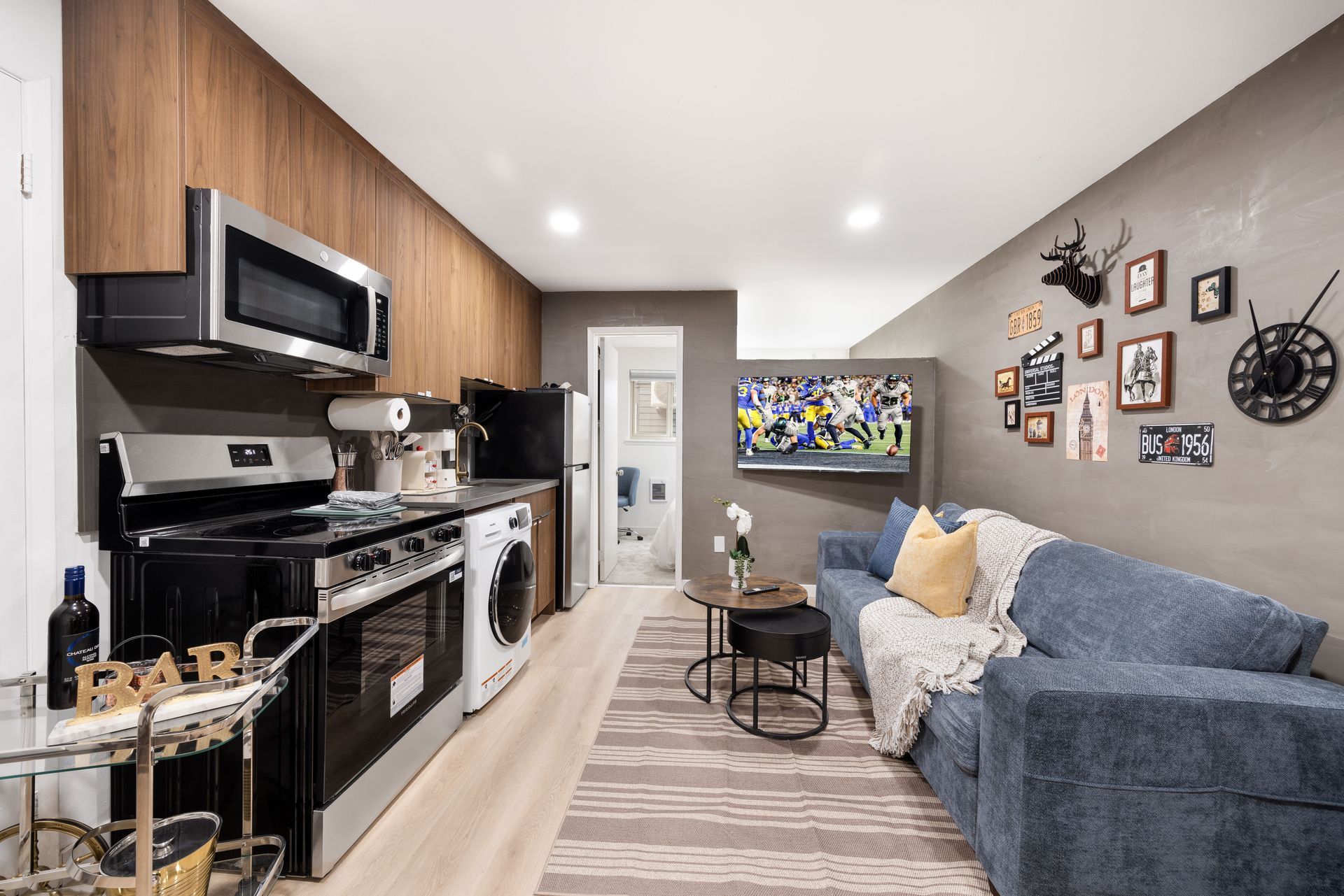 Compact living room with black kitchen cabinets, gray sofa, wall art, and TV on the far wall