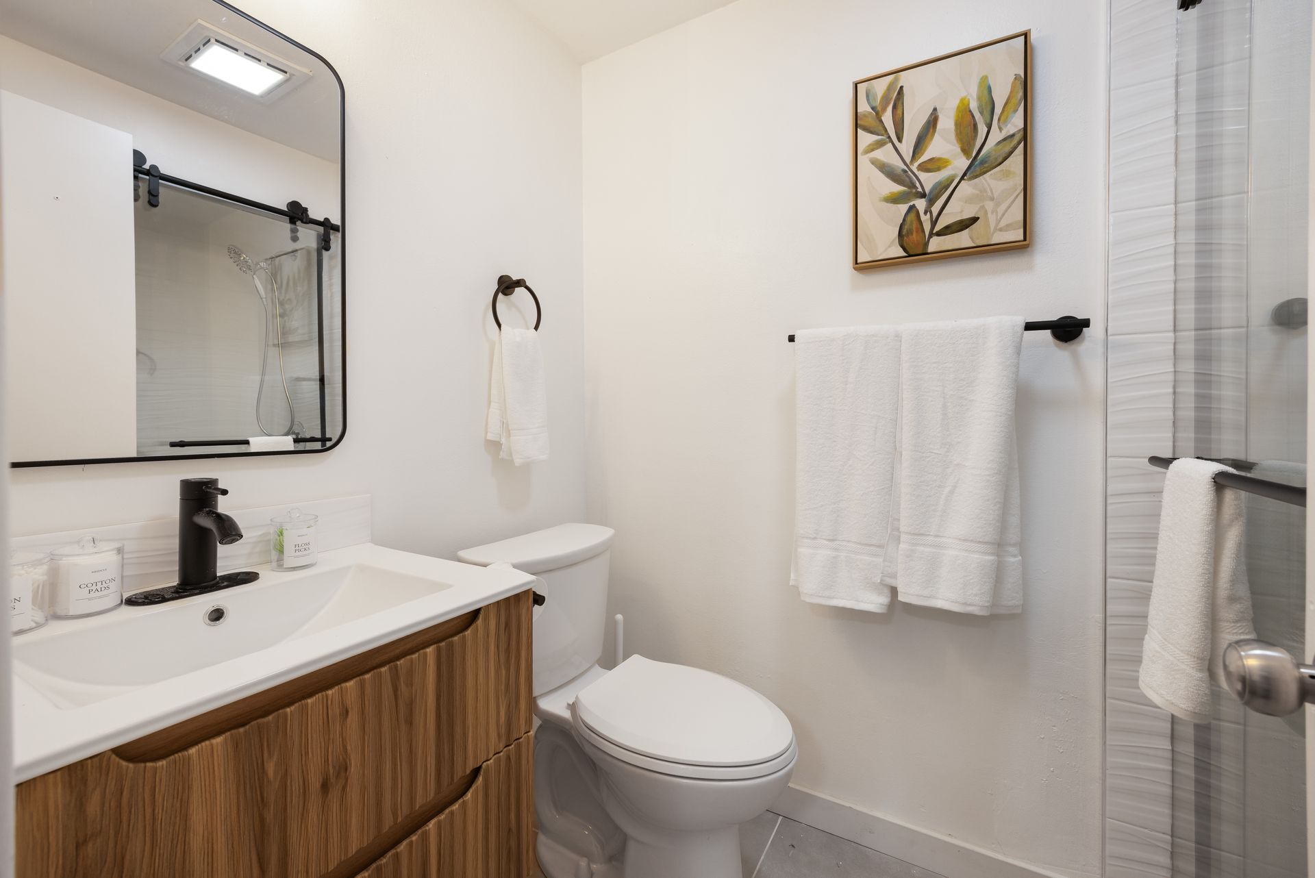 Small bathroom with vanity, toilet, towel rack, shower curtain, and framed wall art
