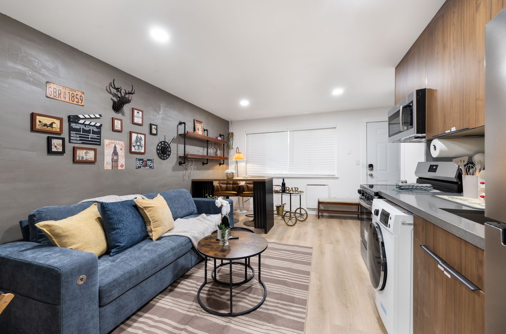 Modern open-plan living room and kitchen with navy sofa, wall art, wood cabinets, and dining nook