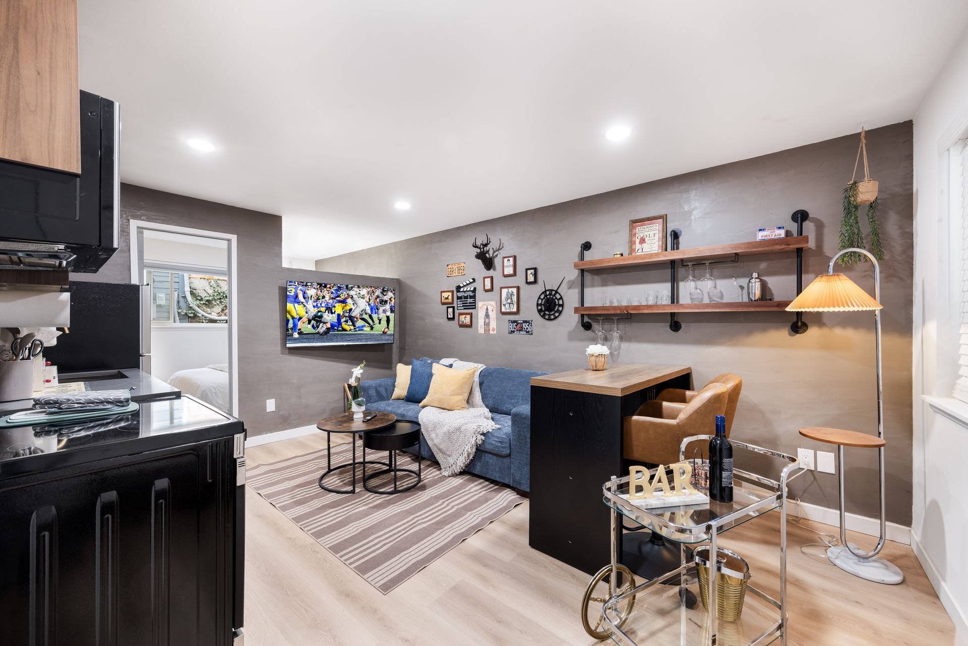 Modern living room with blue sofa, wall-mounted TV, desk, and warm pendant lighting