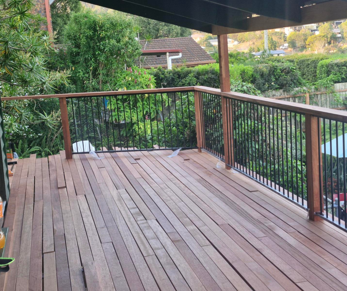 Wooden deck patio with black metal railing, overlooking a garden and neighboring houses. Wooden deck patio with black metal railing, overlooking a garden and neighboring houses.