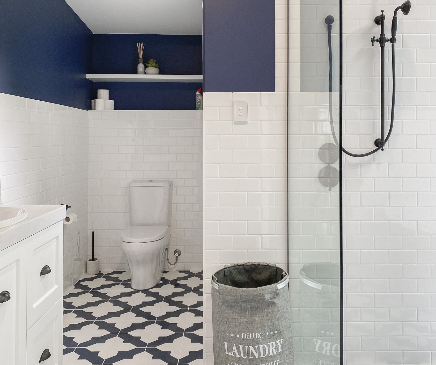 Blue-and-white bathroom with toilet, laundry sink, and glass shower enclosure