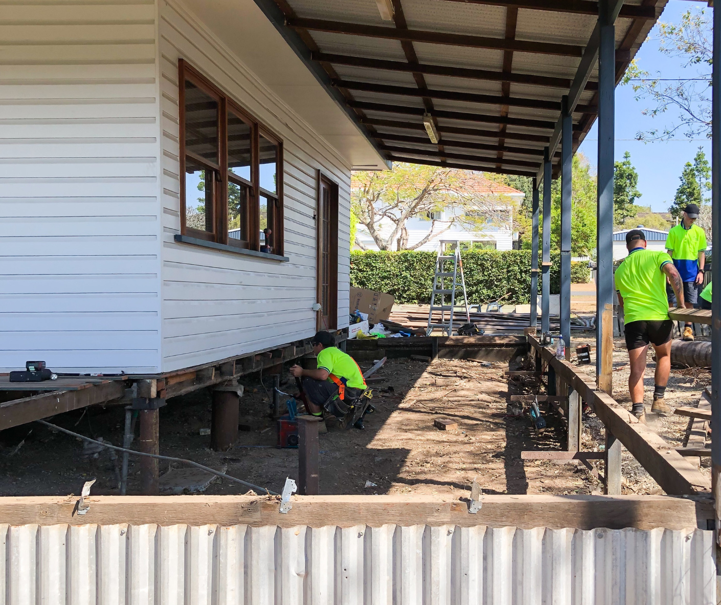 Workers in neon shirts repairing a raised house porch and yard area with dirt and posts Workers in neon shirts repairing a raised house porch and yard area with dirt and posts