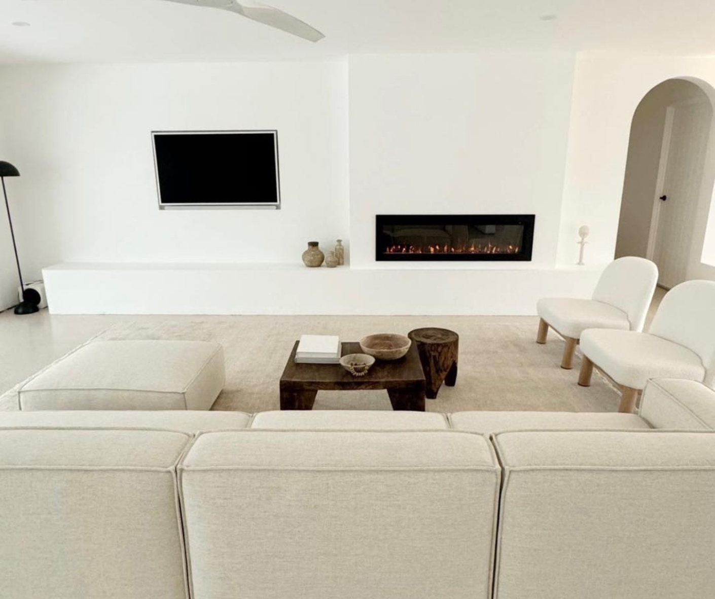 Bright minimalist living room with white sectional, wall-mounted TV, and long fireplace