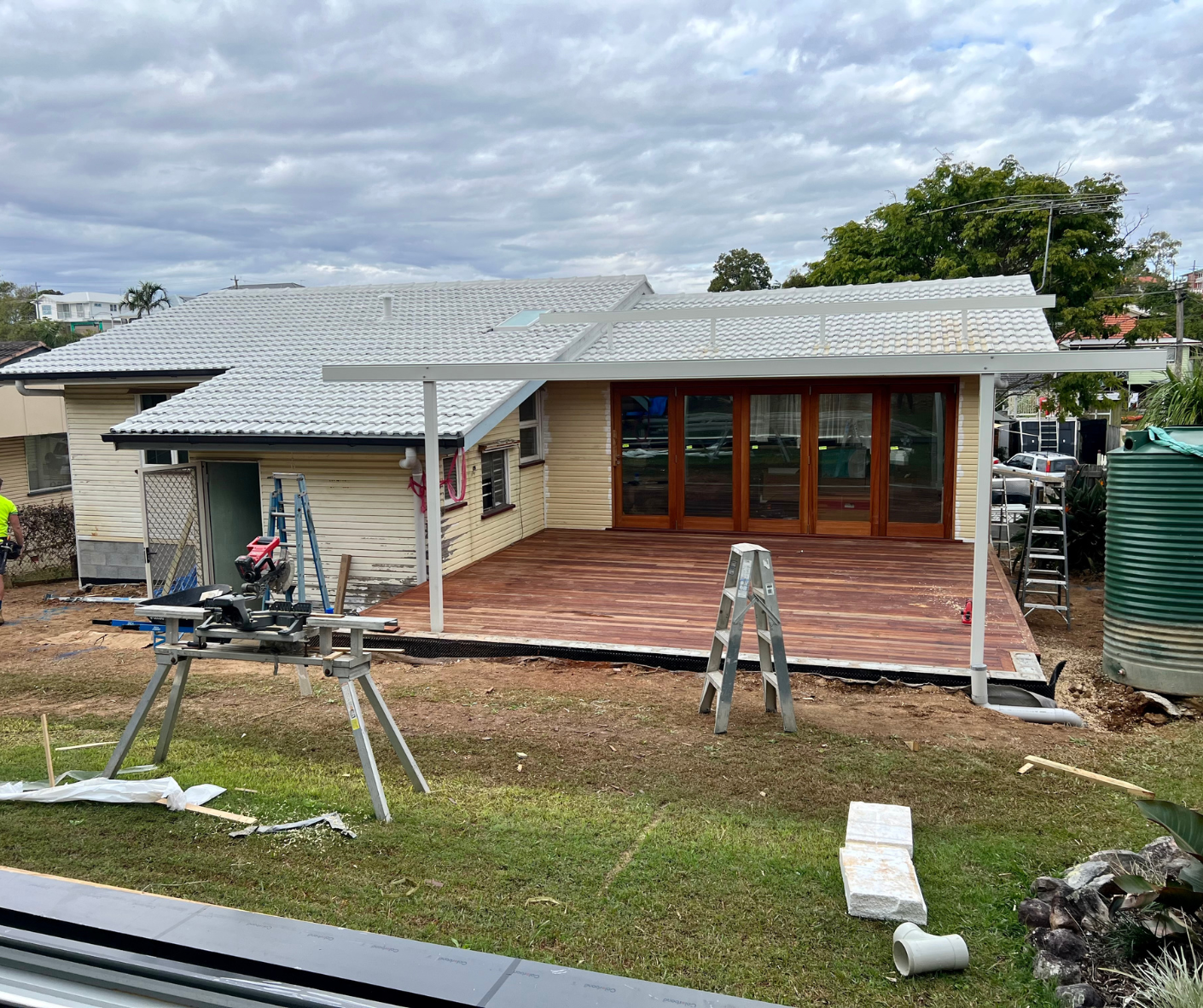 House exterior with a new wooden deck, roof repairs, and construction tools in a yard House exterior with a new wooden deck, roof repairs, and construction tools in a yard