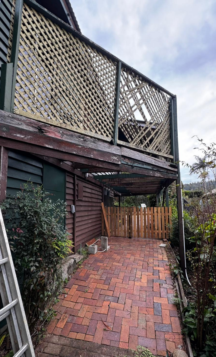 Brick-paved side yard beside a dark wood house with a lattice balcony and fenced gate under a cloudy sky Brick-paved side yard beside a dark wood house with a lattice balcony and fenced gate under a cloudy sky