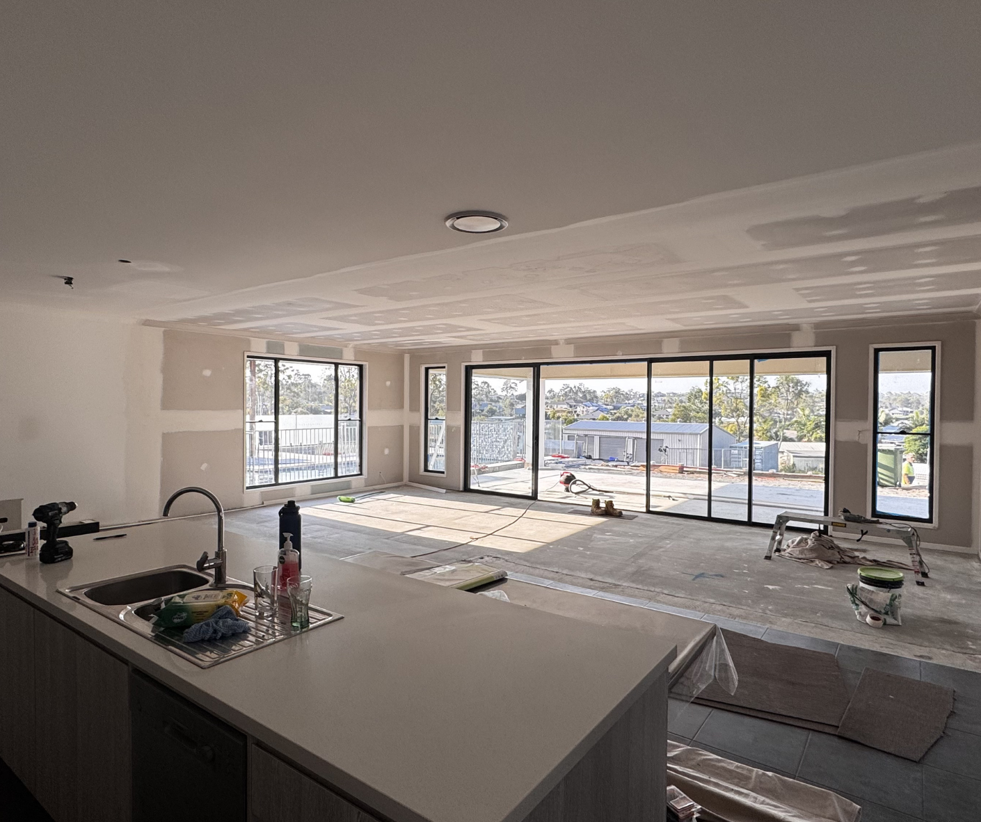 Modern open-plan kitchen overlooking a bright living room with large sliding glass doors to a patio and pool.