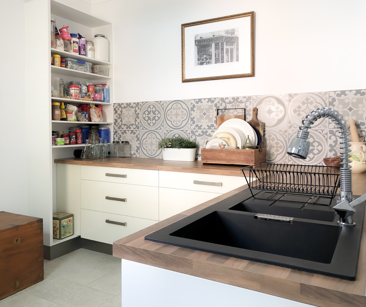 Bright kitchen with black sink, tiled backsplash, open pantry shelves, and countertop appliances Bright kitchen with black sink, tiled backsplash, open pantry shelves, and countertop appliances