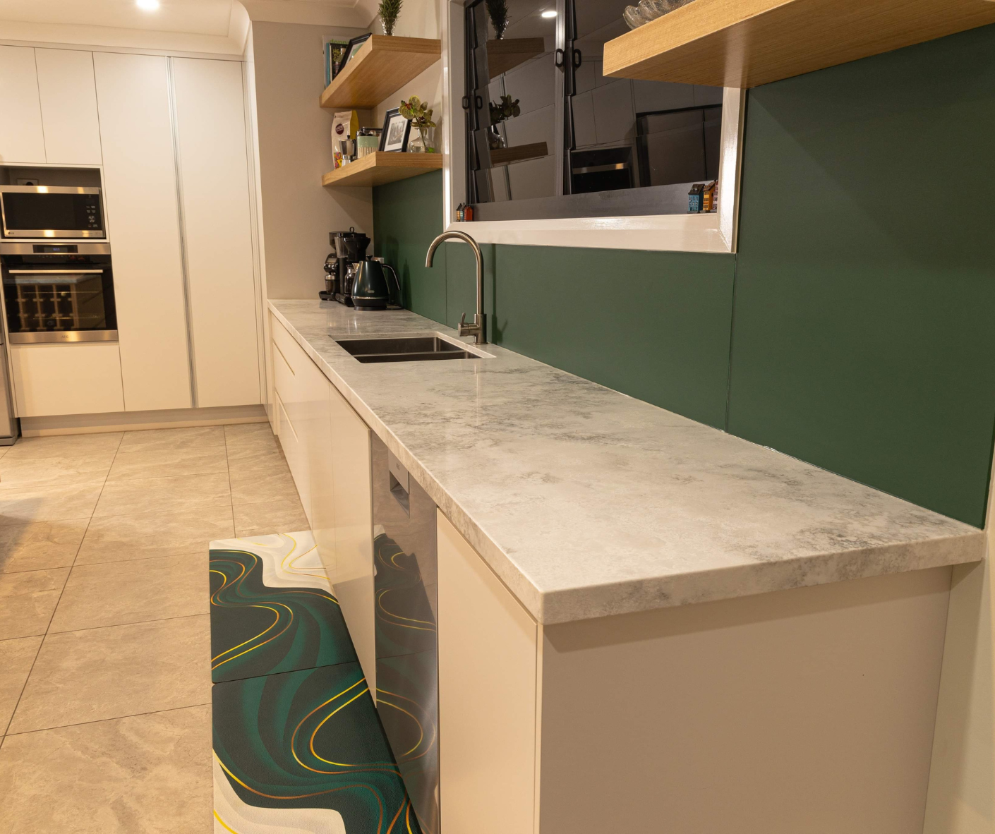 Modern kitchen with white counters, green backsplash, and a patterned rug near a built-in oven. Modern kitchen with white counters, green backsplash, and a patterned rug near a built-in oven.