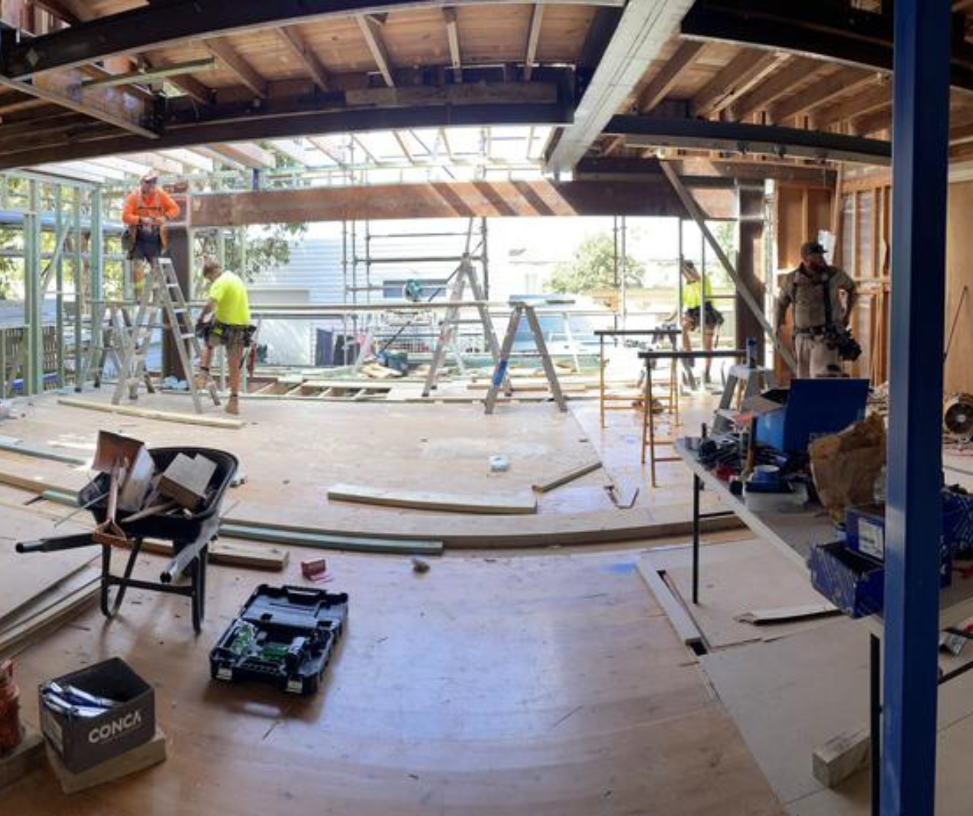 Construction site interior with workers, tools, and open framing under a partially built roof Construction site interior with workers, tools, and open framing under a partially built roof