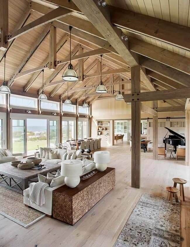Spacious rustic living room with vaulted wood beams, large windows, and a central sofa display