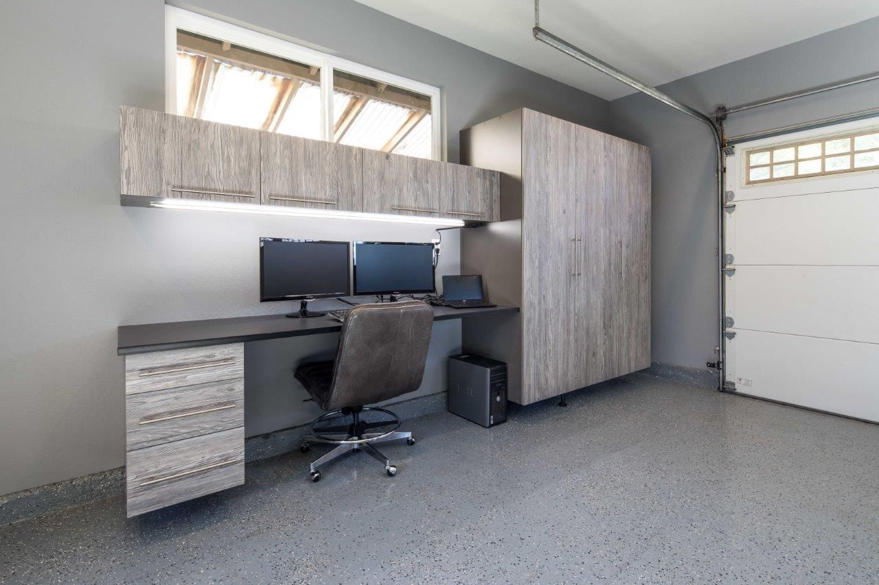 Modern home office with desk, dual monitors, chair, storage cabinet, and gray carpet.