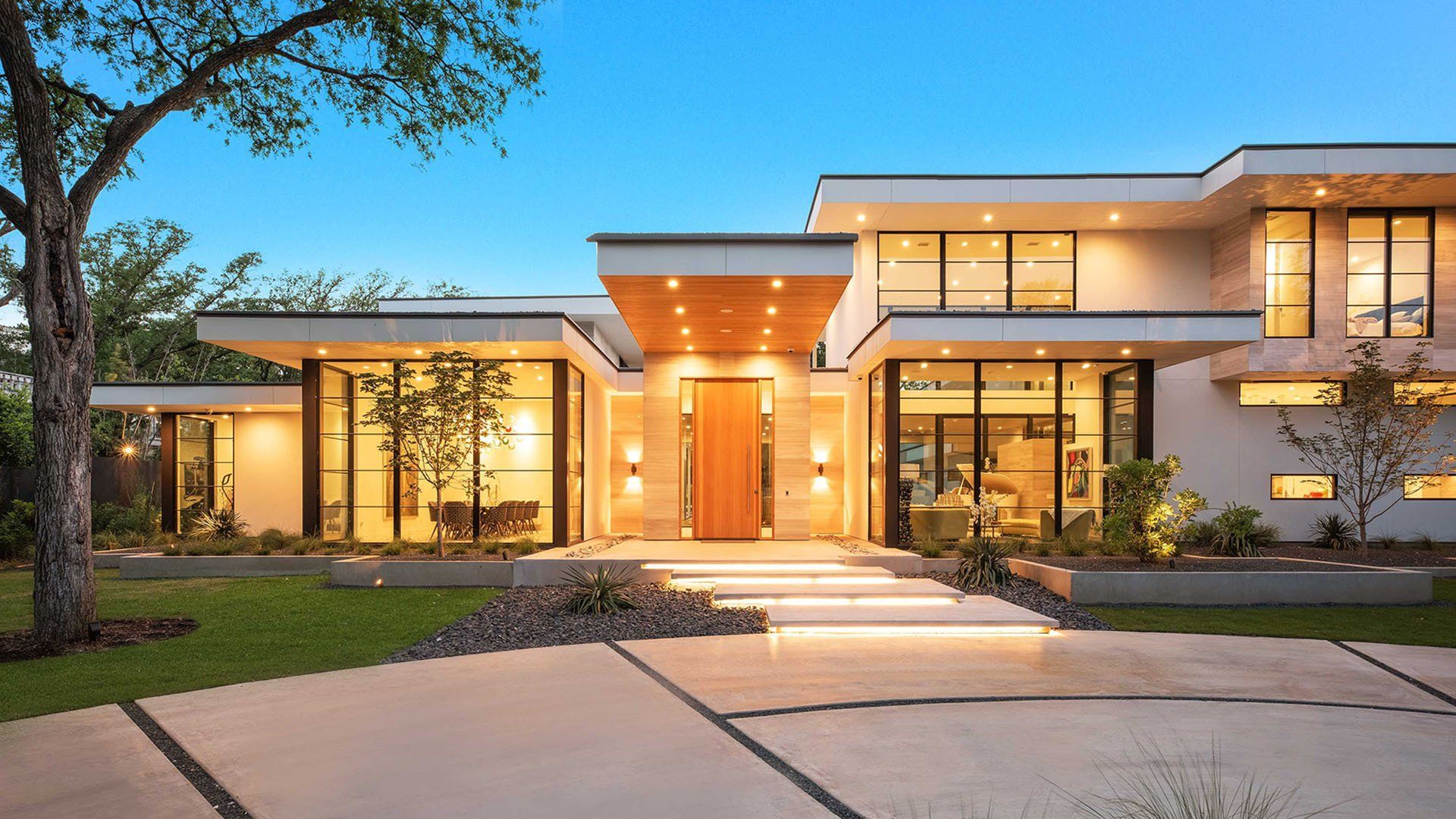 Modern two-story home at dusk with warm exterior lights and a landscaped front yard