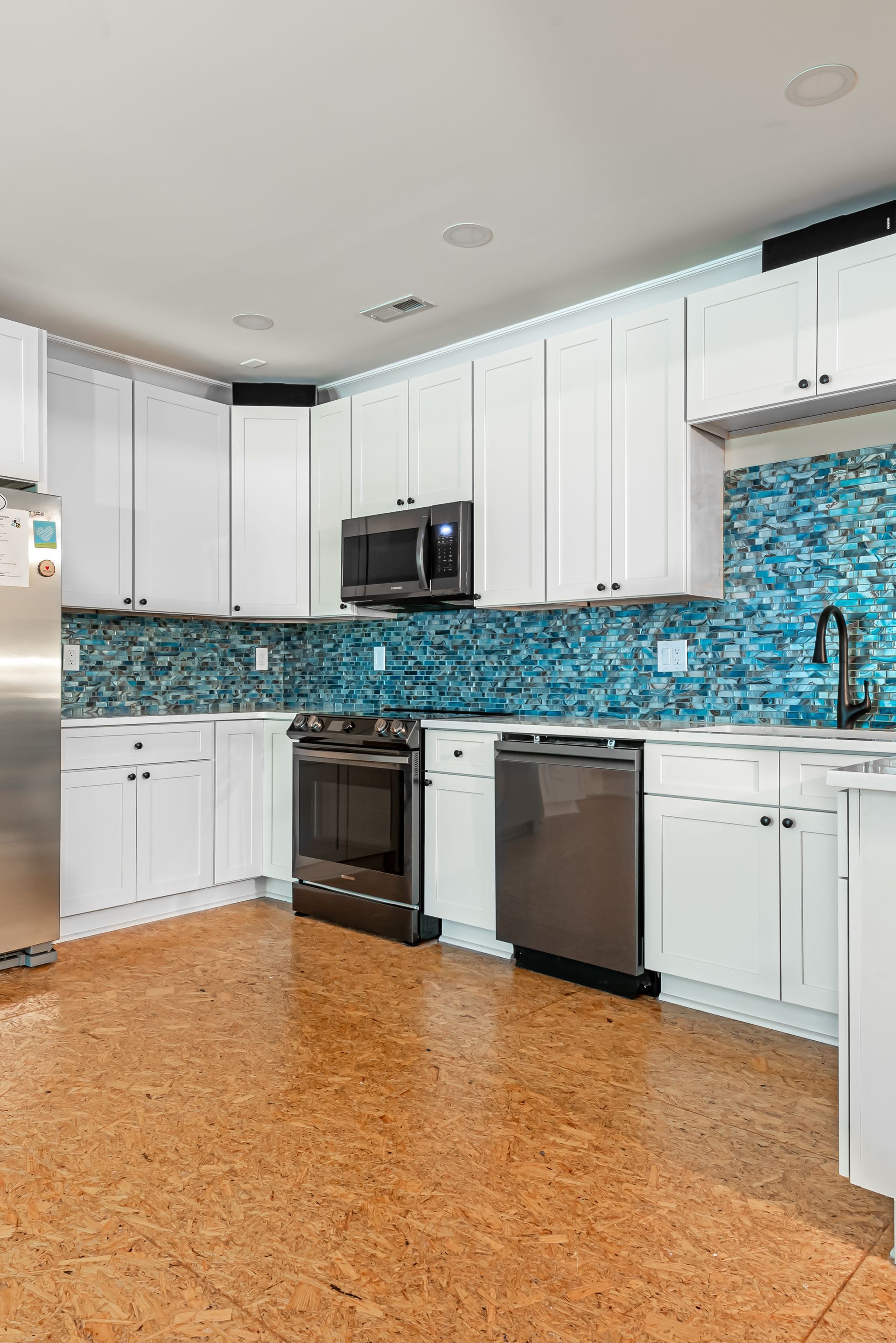 Modern white kitchen with turquoise mosaic backsplash, stainless appliances, and cork flooring