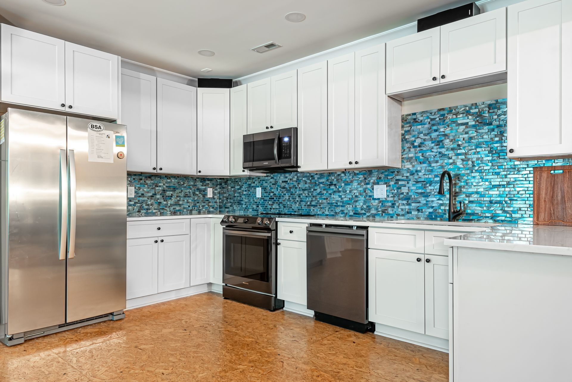 Bright modern kitchen with white cabinets, stainless appliances, and blue mosaic backsplash.