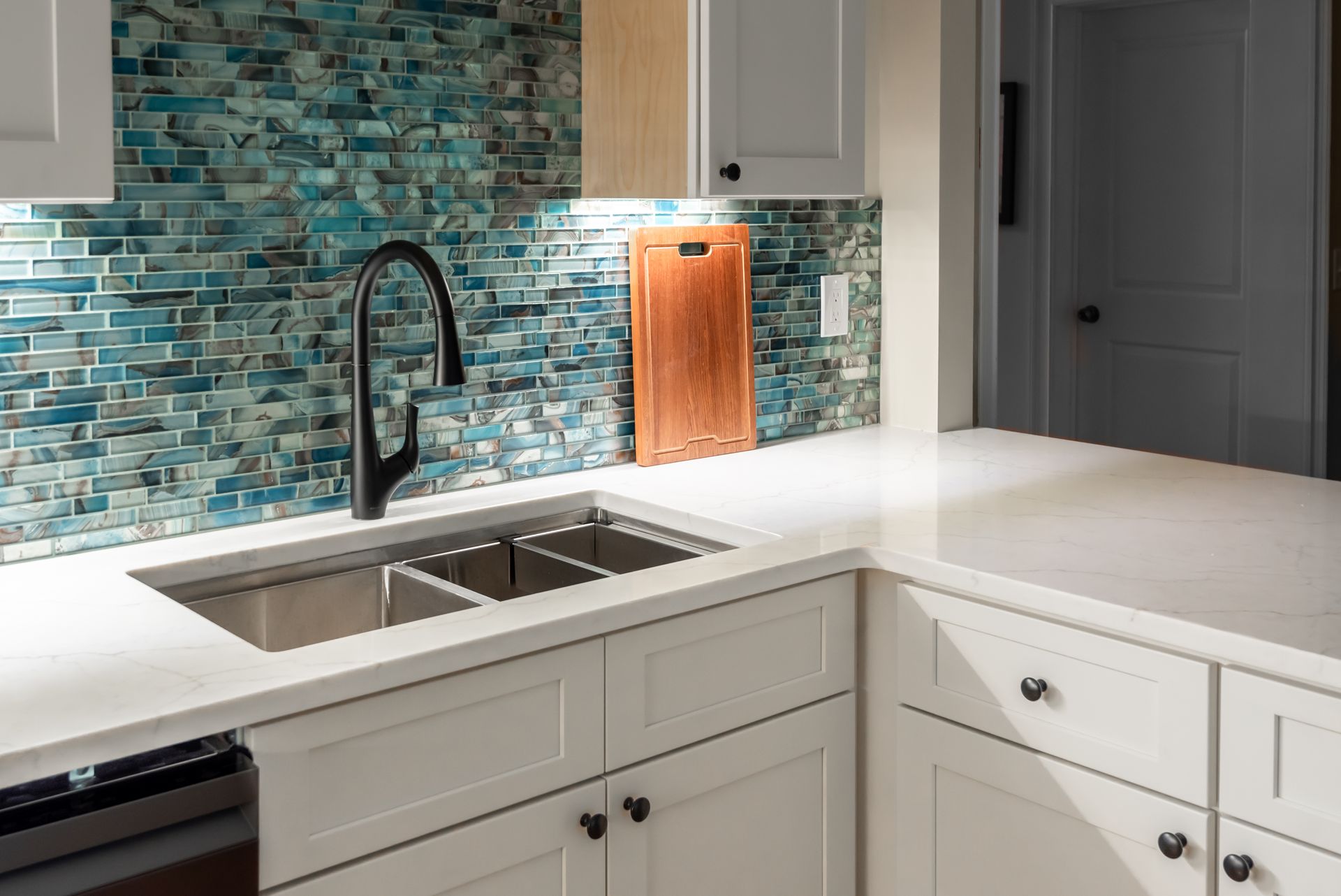 Modern kitchen sink with black faucet, white cabinets, and blue mosaic tile backsplash