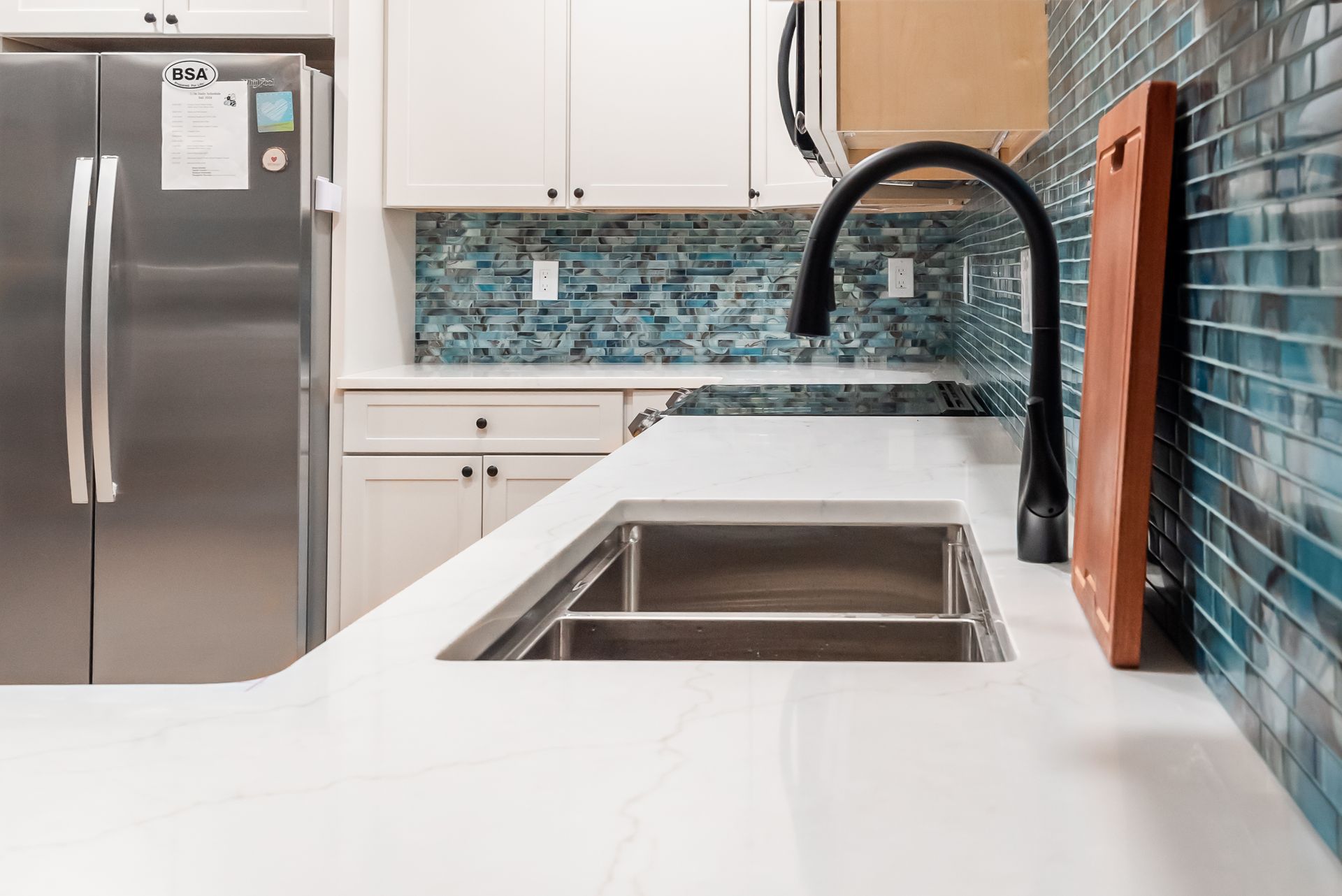 Modern kitchen with stainless steel appliances, white cabinets, blue tile backsplash, and a large island sink