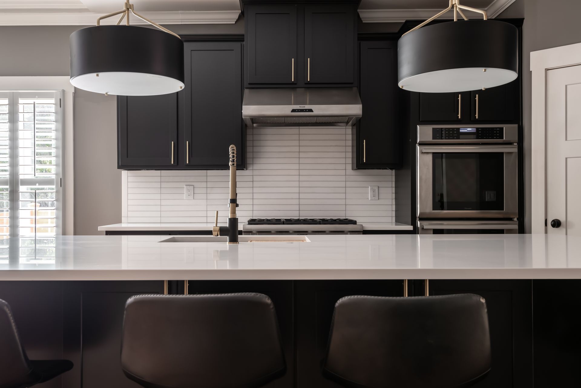 Modern kitchen with black cabinets, white island, and two pendant lights over a sink.