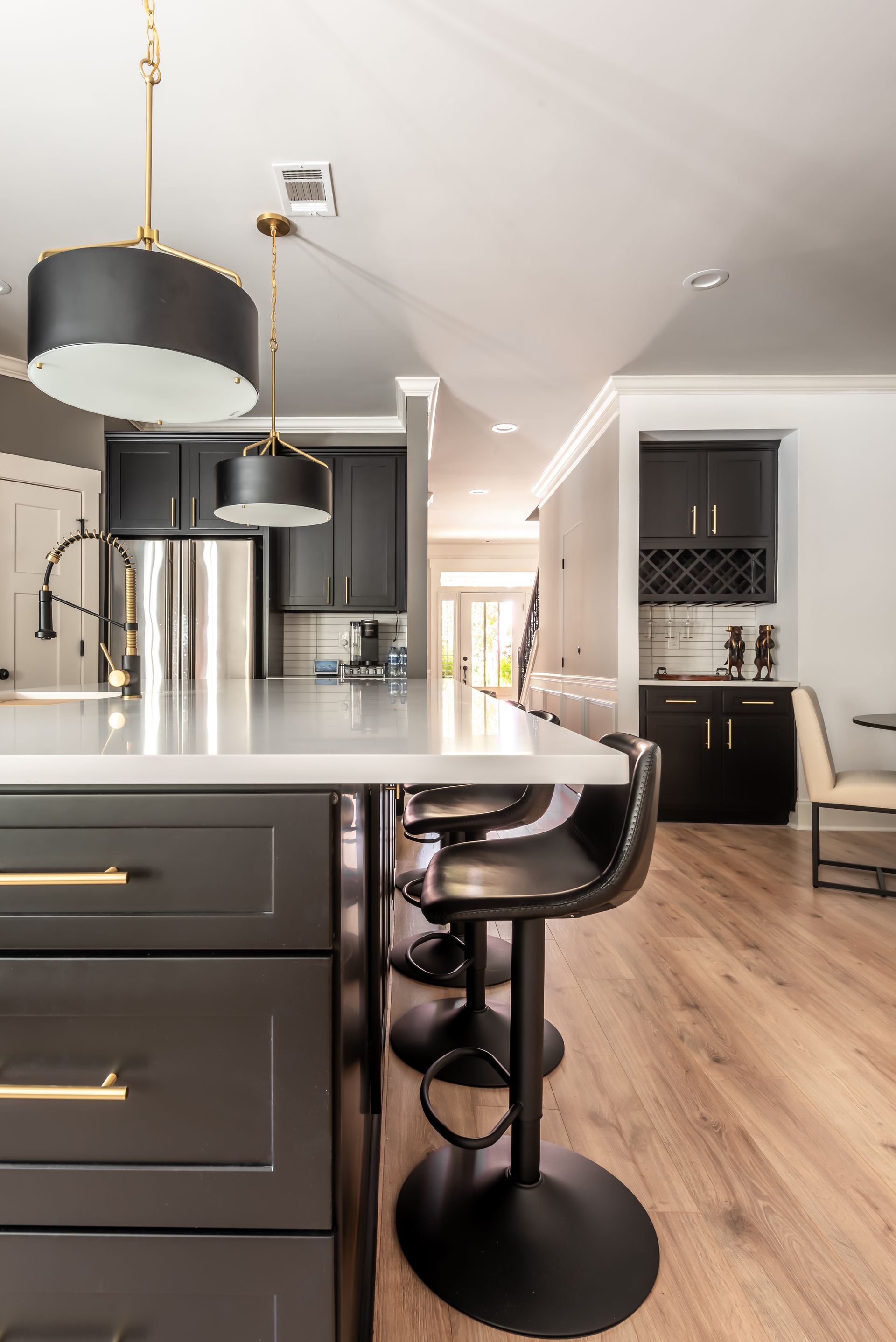 Modern kitchen with dark cabinets, white island, stainless appliances, and a black bar stool in the foreground