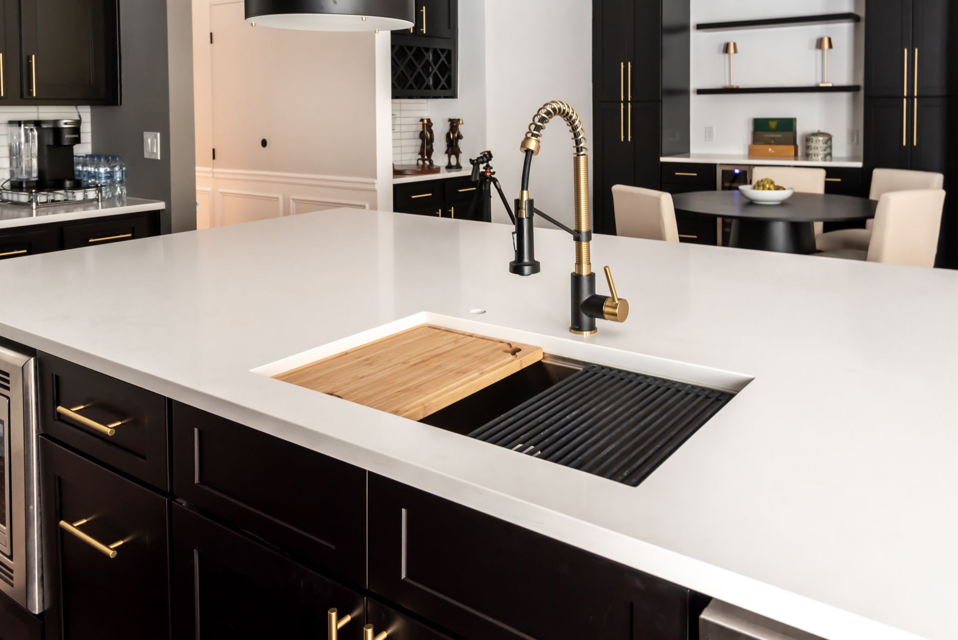 Modern kitchen island with white countertop, black cabinets, brass faucet, and built-in sink and cooktop