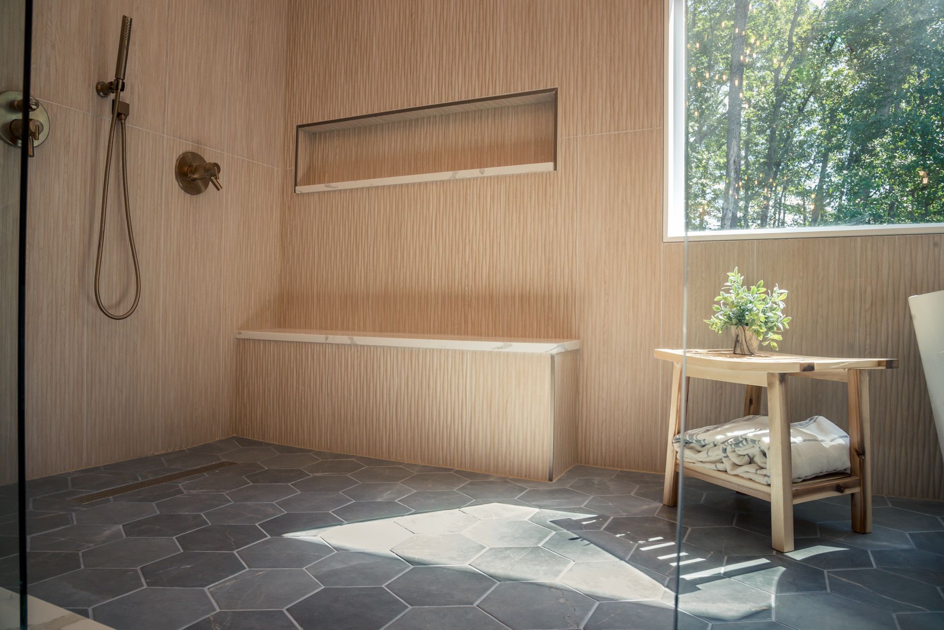 Minimalist wooden interior with a bench, hanging towel, small plant table, and window light on stone floor.