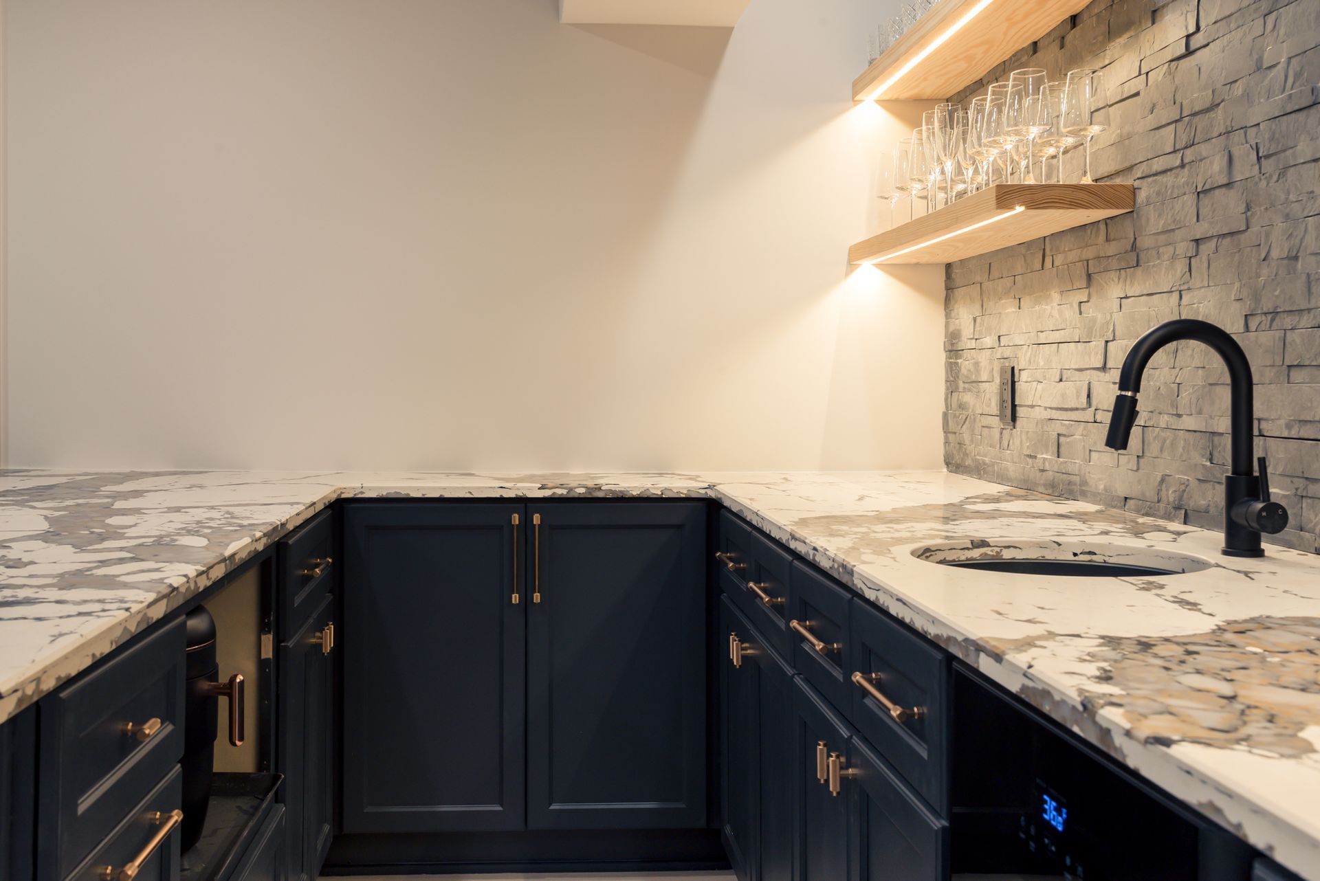 Modern kitchen with dark cabinets, marble countertops, black faucet, and brick accent wall under warm lighting