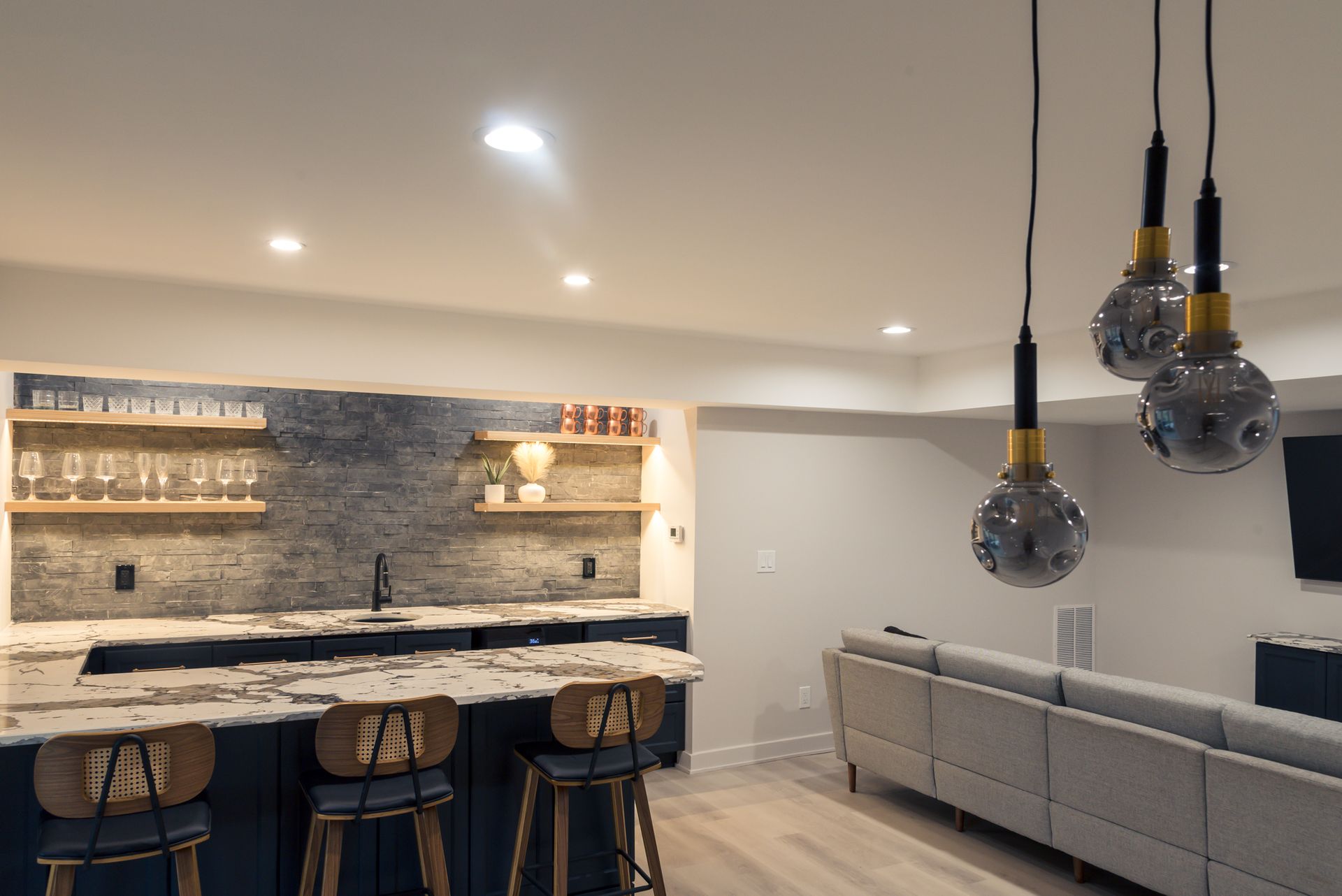 Modern open-concept kitchen and living area with stone island, barstools, gray sofa, and hanging pendant lights