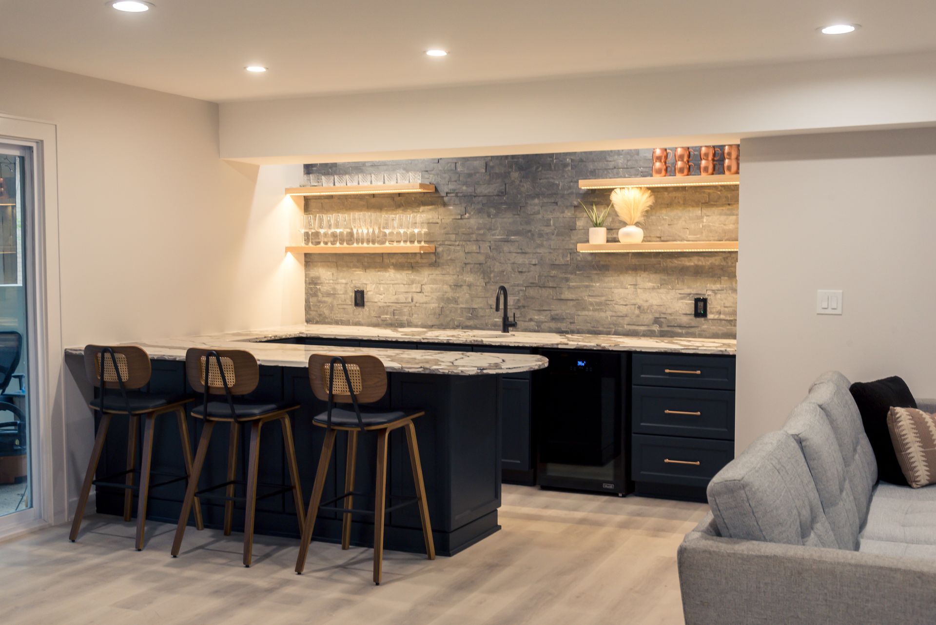 Modern open-concept kitchen with dark island stools, marble counters, and a gray sofa nearby
