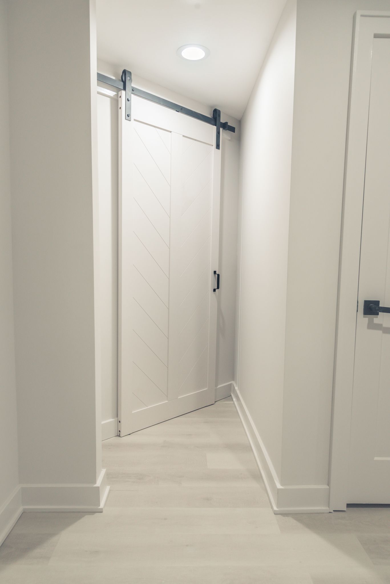 Narrow hallway with white walls, light wood floors, and a closed white double-door ahead