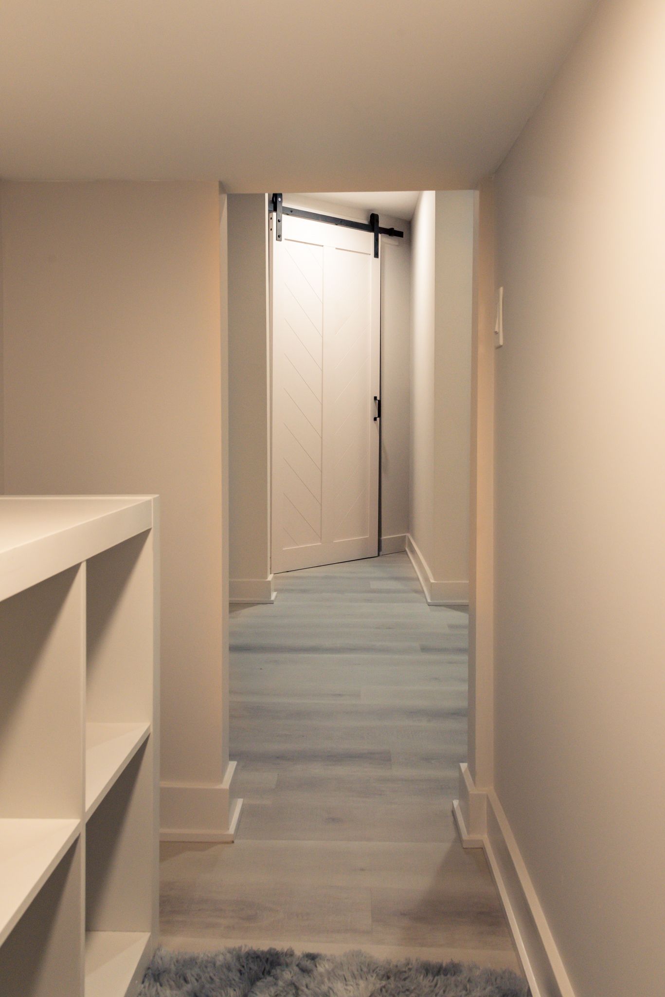 Narrow hallway with beige walls, light wood floor, and an open door at the end