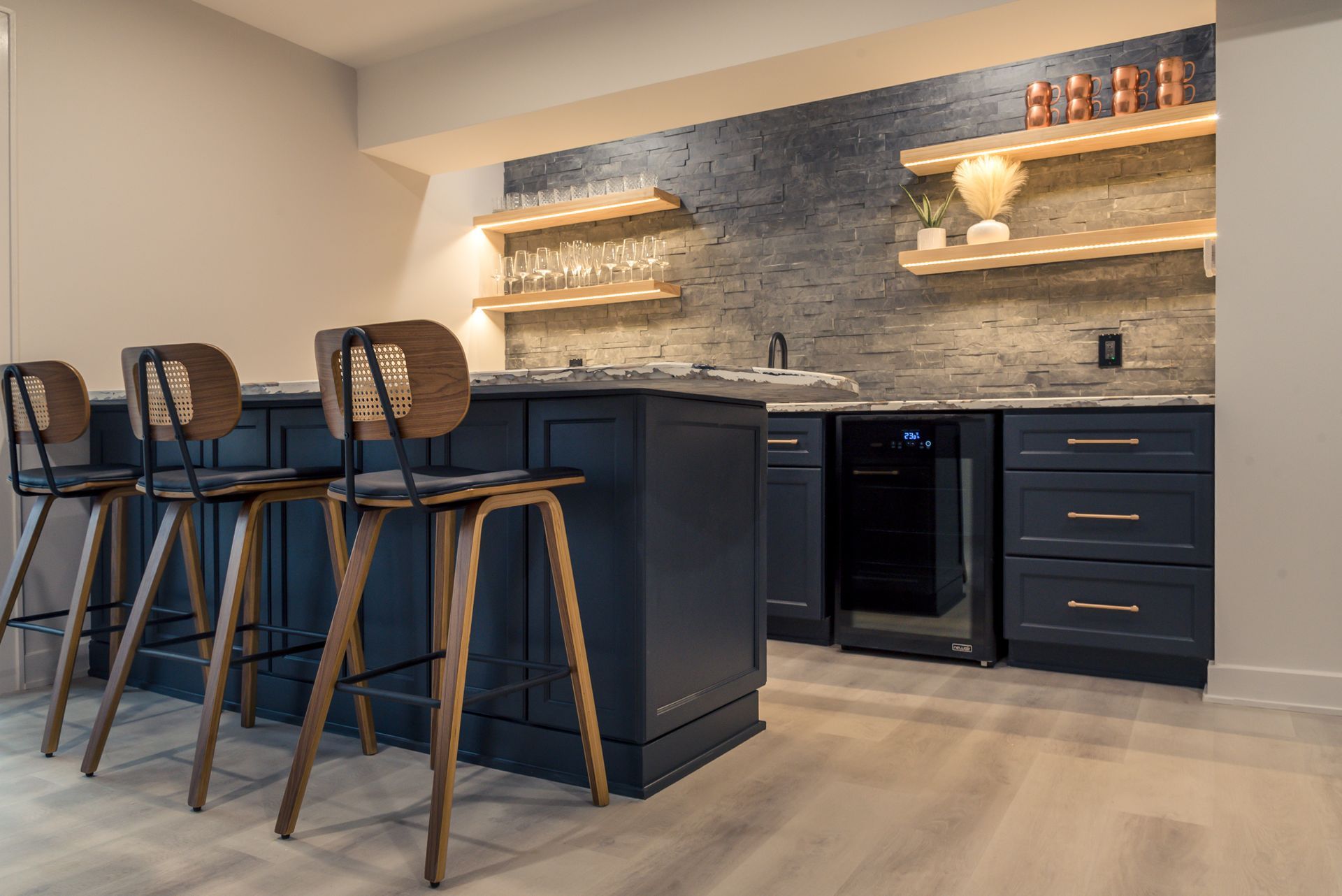 Modern kitchen with dark island stools, navy cabinets, and under-shelf lighting by a tiled backsplash