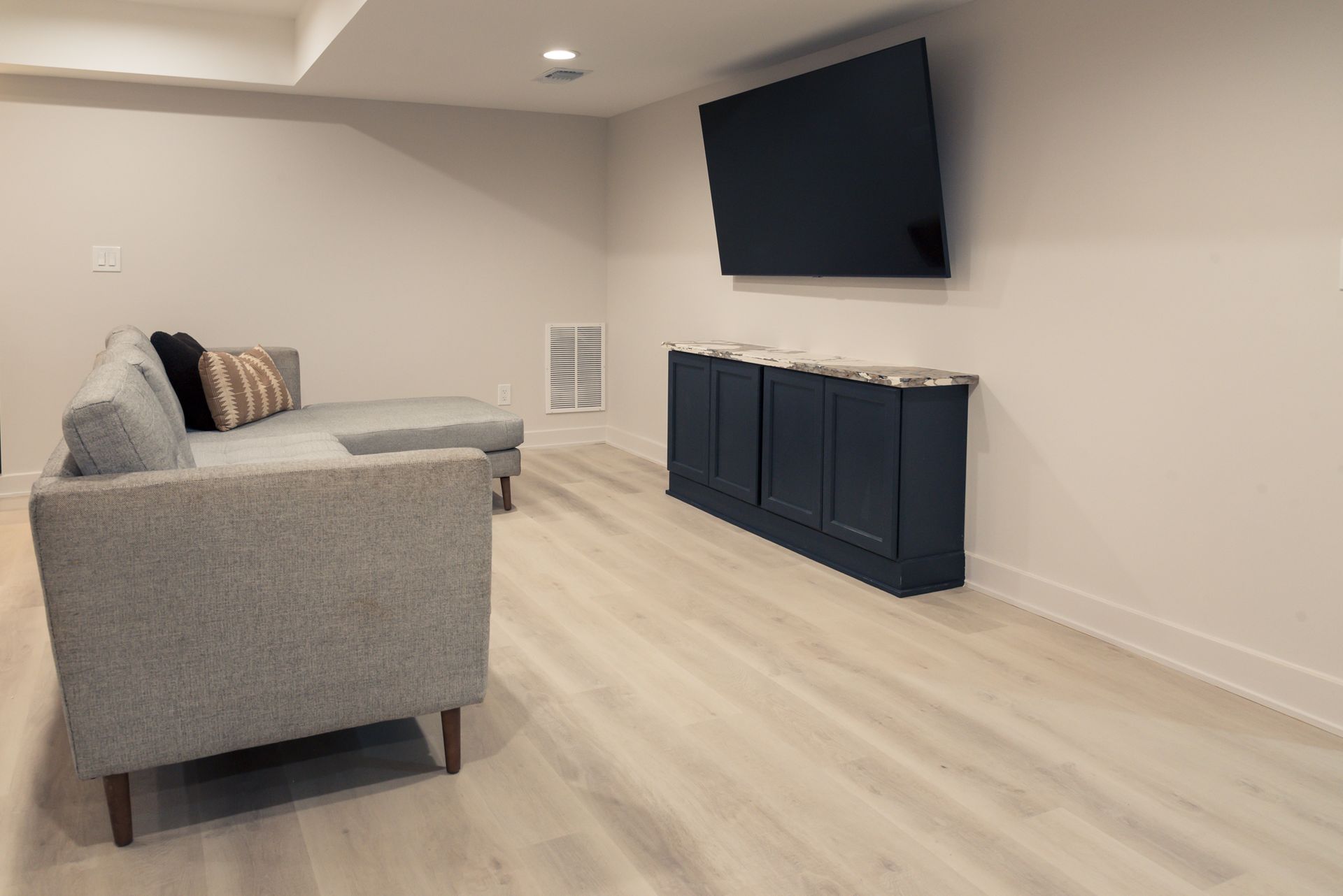 Minimal living room with gray sofa, wall-mounted TV, and dark cabinet on light wood floor.