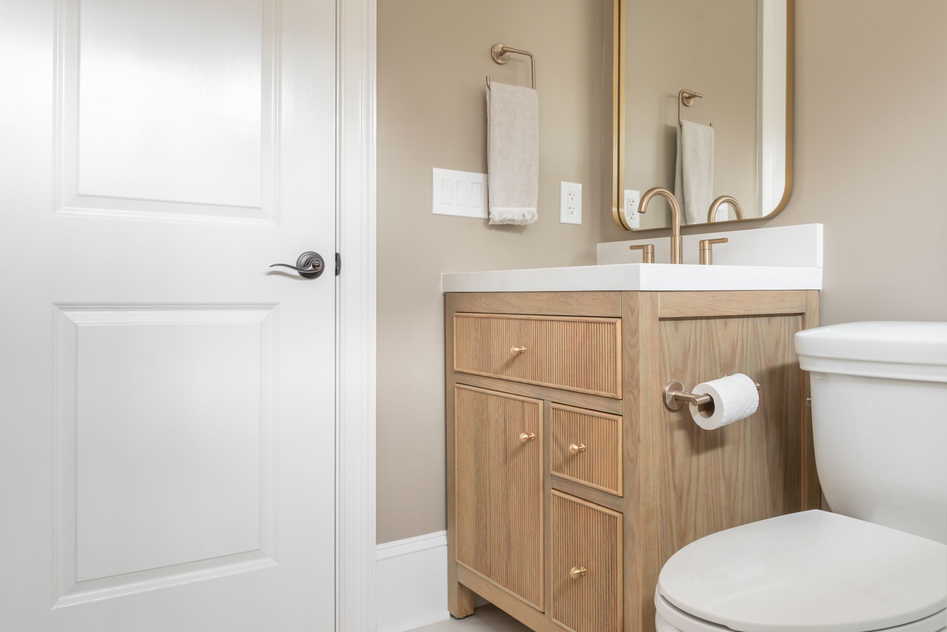 Modern bathroom with white door, wood vanity, mirror, and toilet.