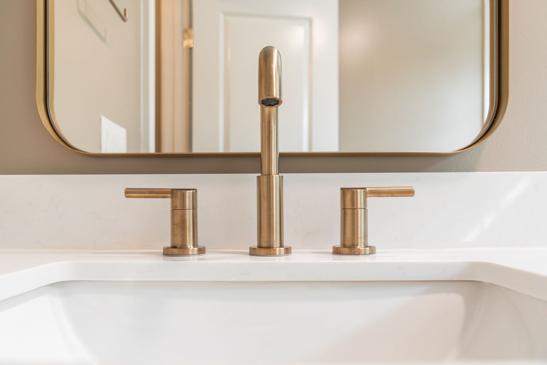 Modern bathroom sink with gold faucet and matching handles beneath a mirror