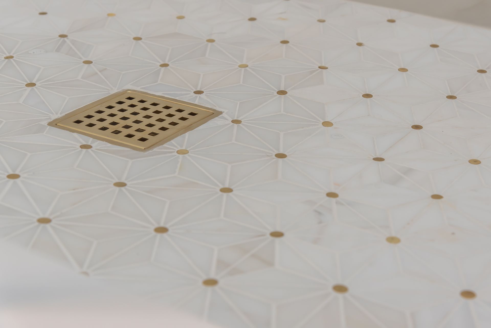 White tiled shower floor with a square beige drain cover and small tan accents