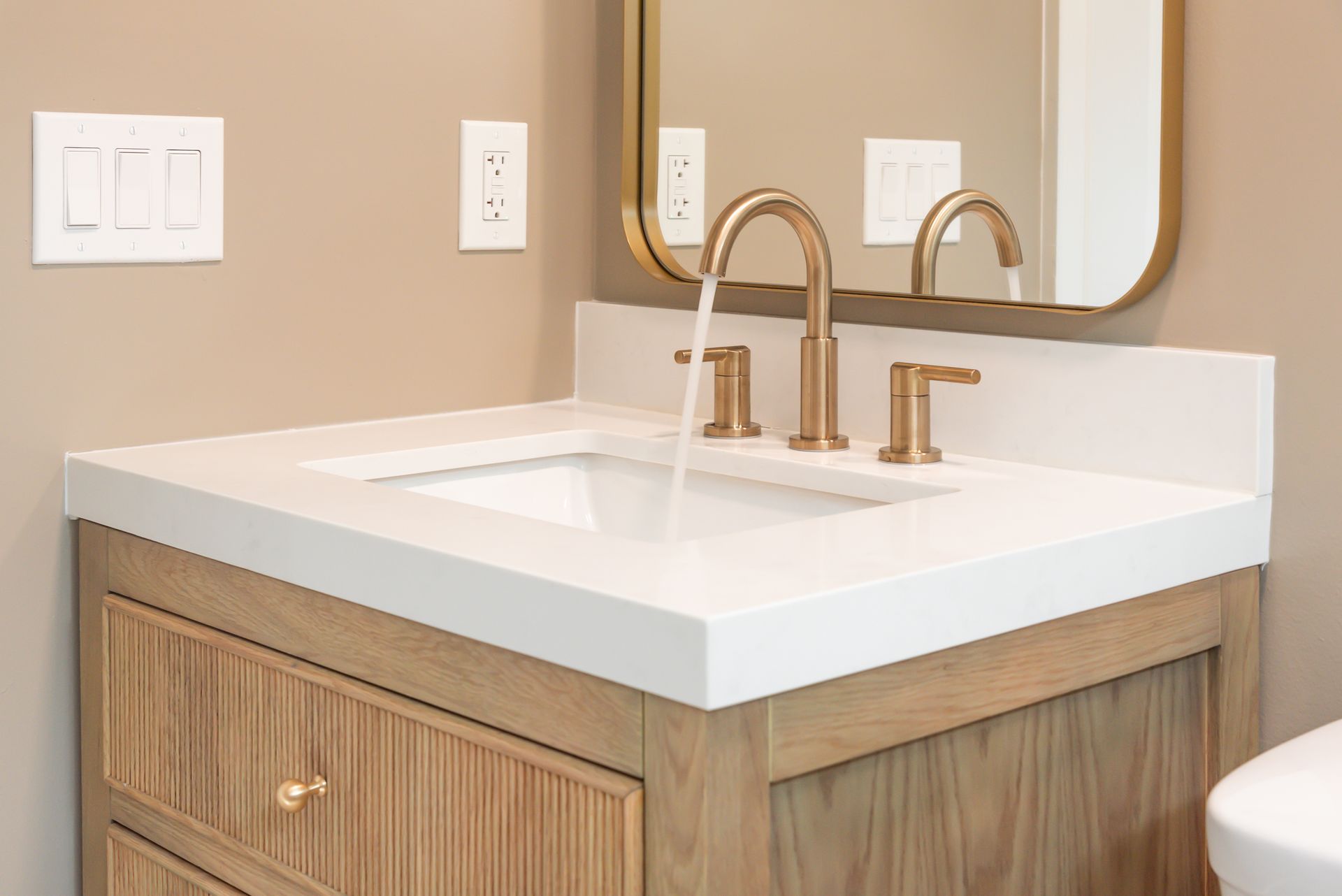 Modern bathroom vanity with white sink, gold faucet, and wood cabinet under a mirror