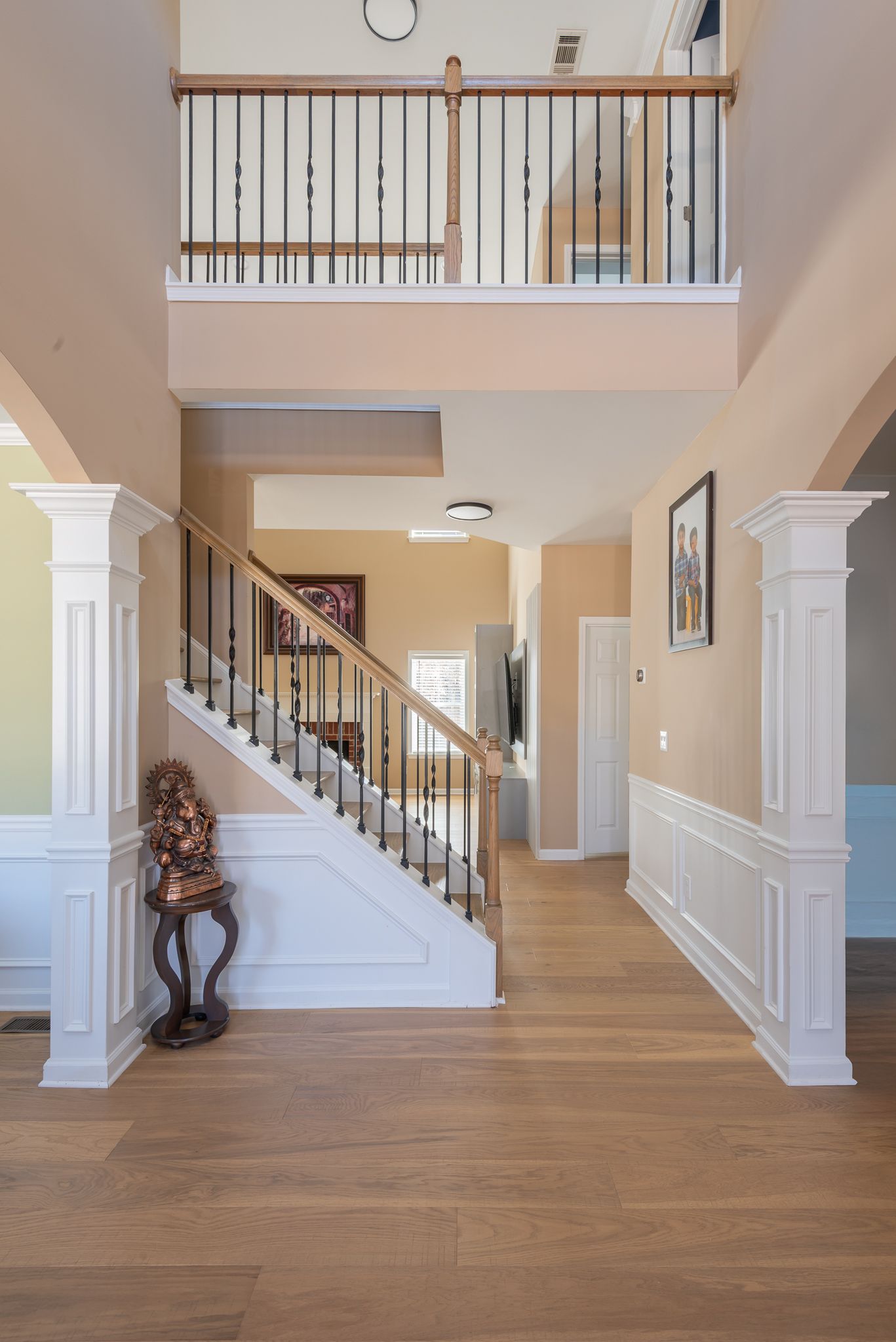 Bright foyer with white staircase, balcony railing, and hardwood floors in a beige home.
