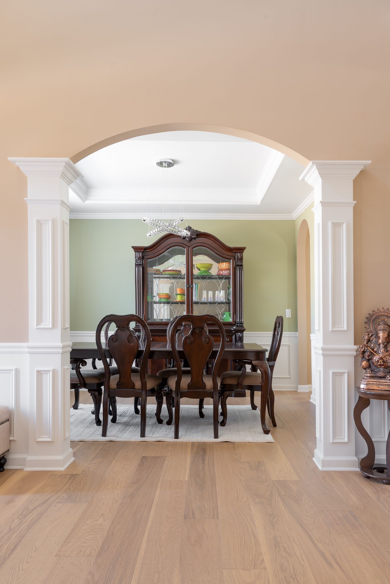 Elegant dining room with dark wood table and chairs, arched opening, and white columns with beige walls