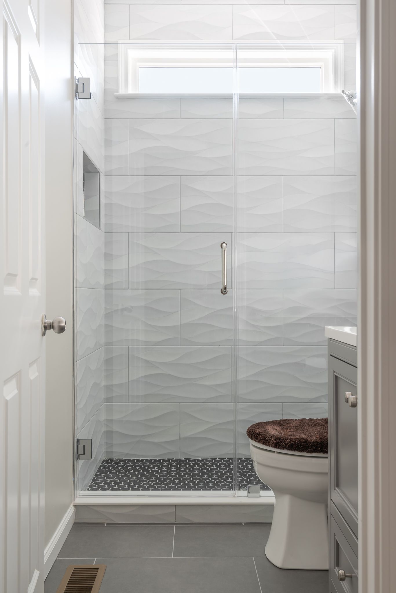 Small white bathroom with a glass shower, toilet, and window above the shower.