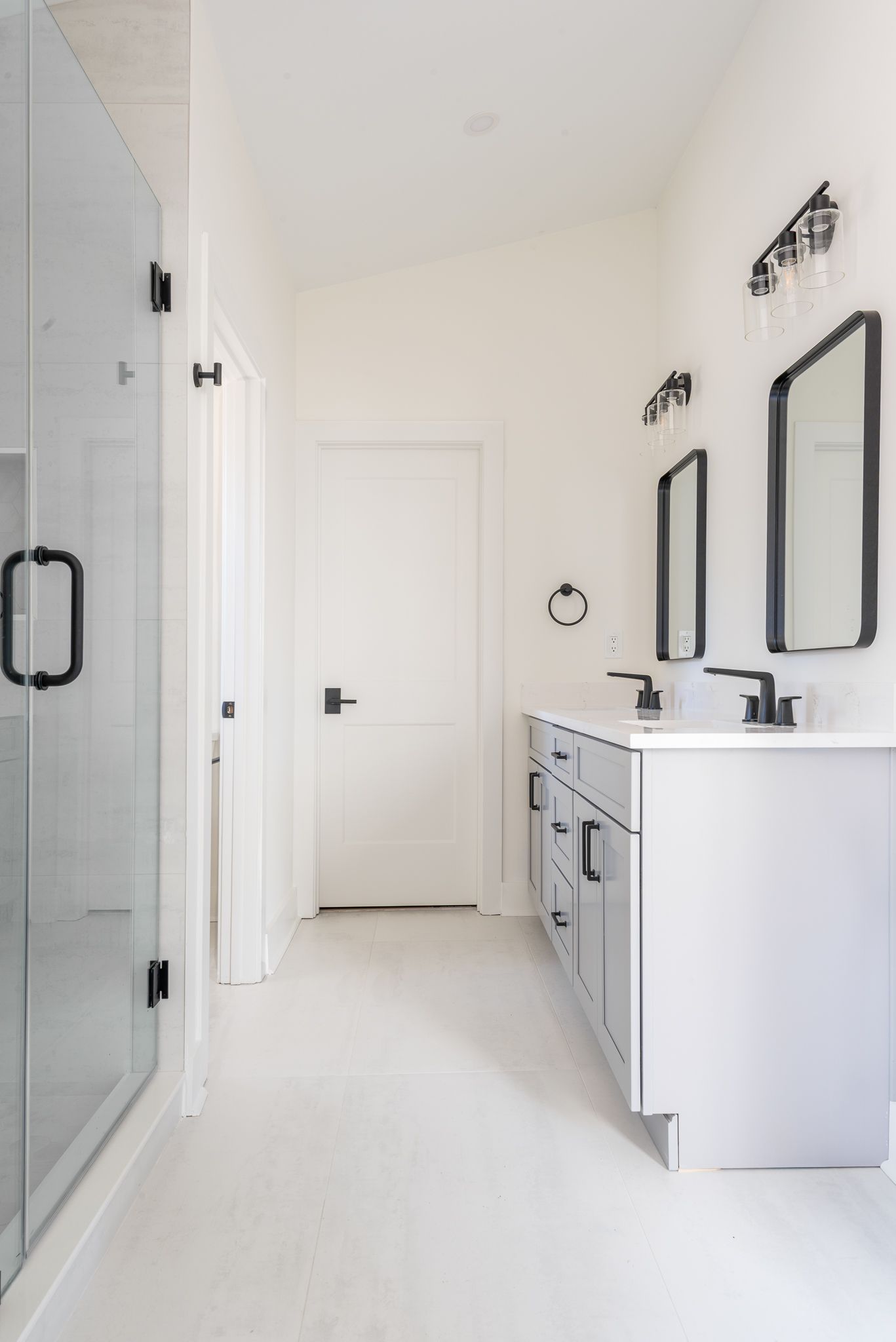 Bright white bathroom with glass shower, double vanity, and black-framed mirrors