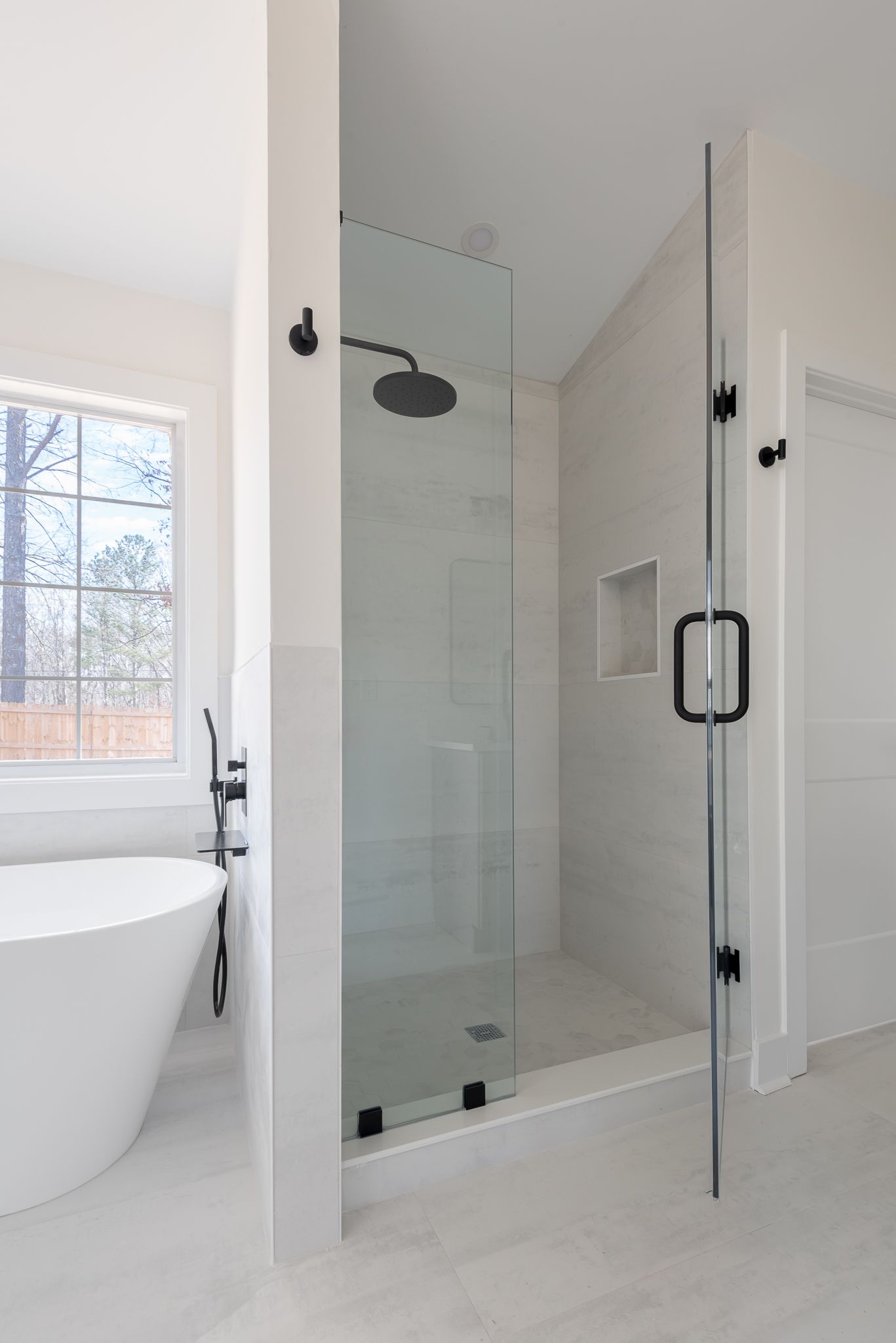 Modern bathroom with glass-enclosed shower, white tub, and bright window
