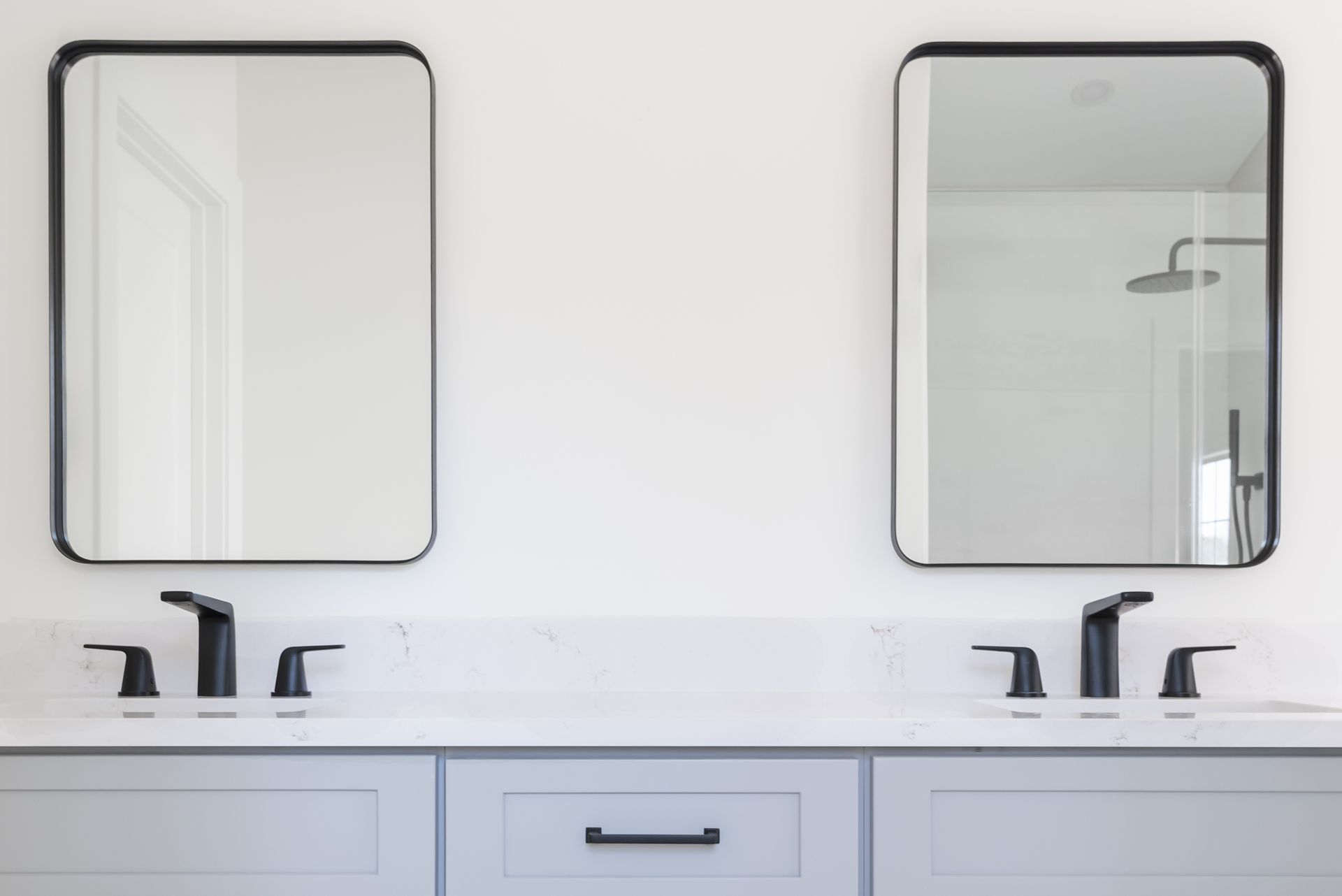 Minimalist bathroom vanity with two black faucets and framed mirrors above a white counter