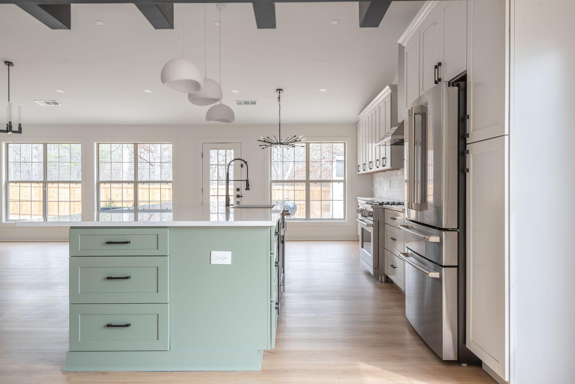 Bright modern kitchen with sage island, stainless appliances, and large windows